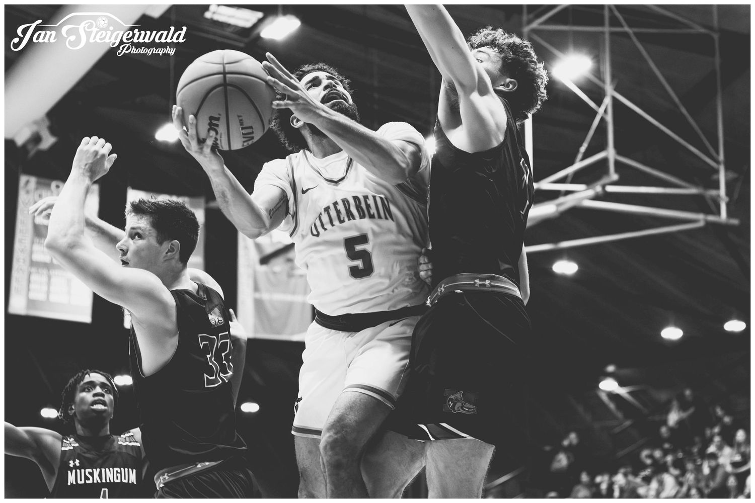 Black and white action shot of a college basketball player with number 5 jersey going up for a shot against defenders.