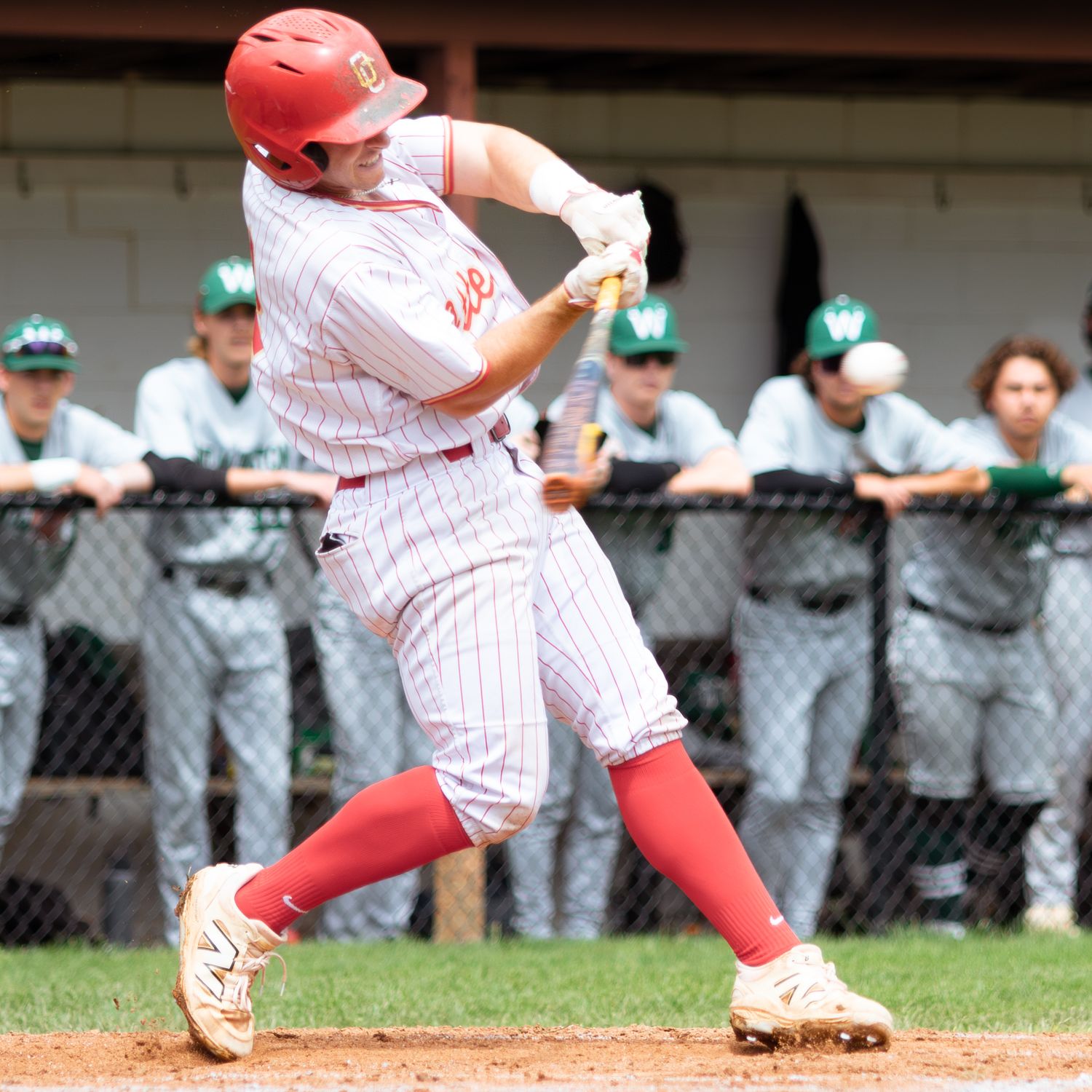 Baseball player in red and white pinstripes slides into base during competitive game against team in green uniforms.