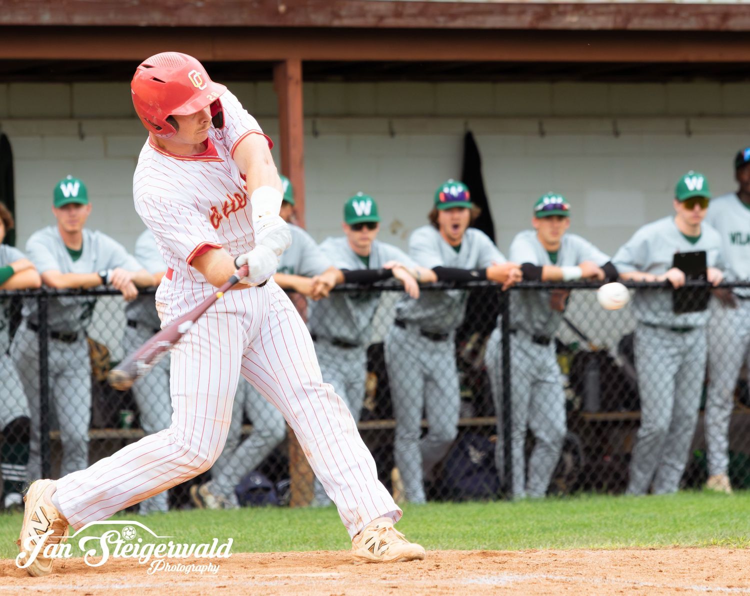 Baseball player in white pinstripe uniform makes solid contact with pitch during competitive game.