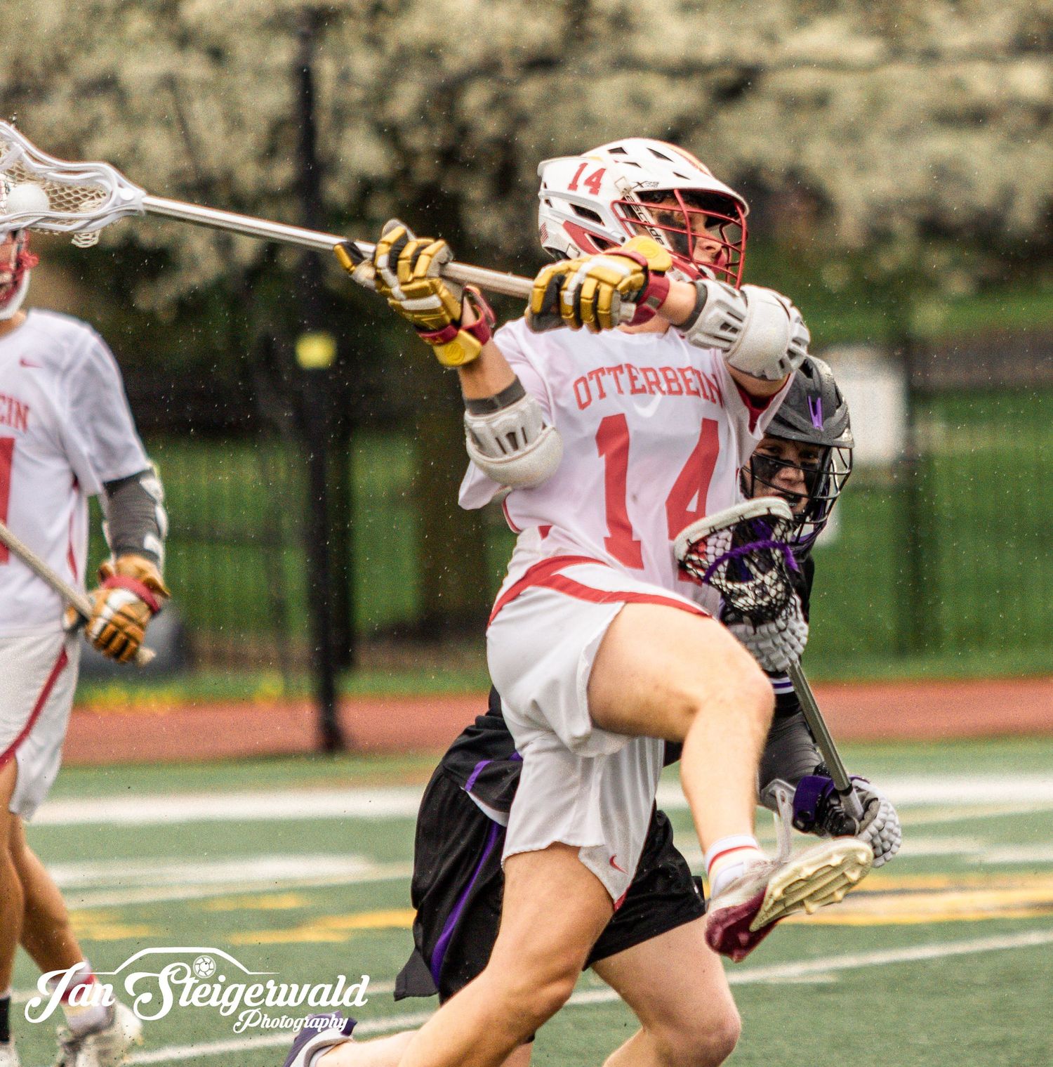 College lacrosse players in white uniforms compete against opponents in dark jerseys during an intense match.