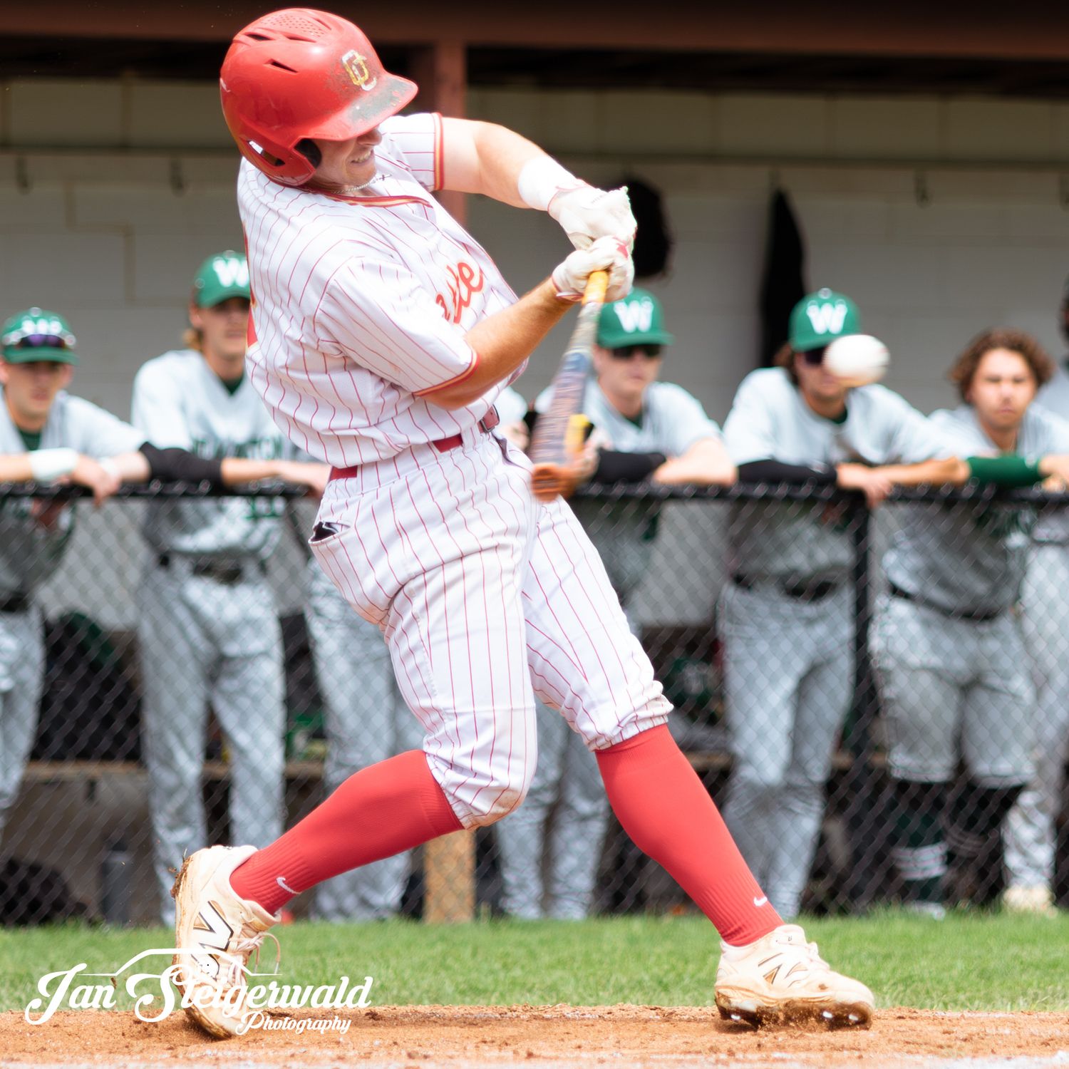 Baseball player slides into base with red uniform during game while opposing team in green watches closely from dugout.