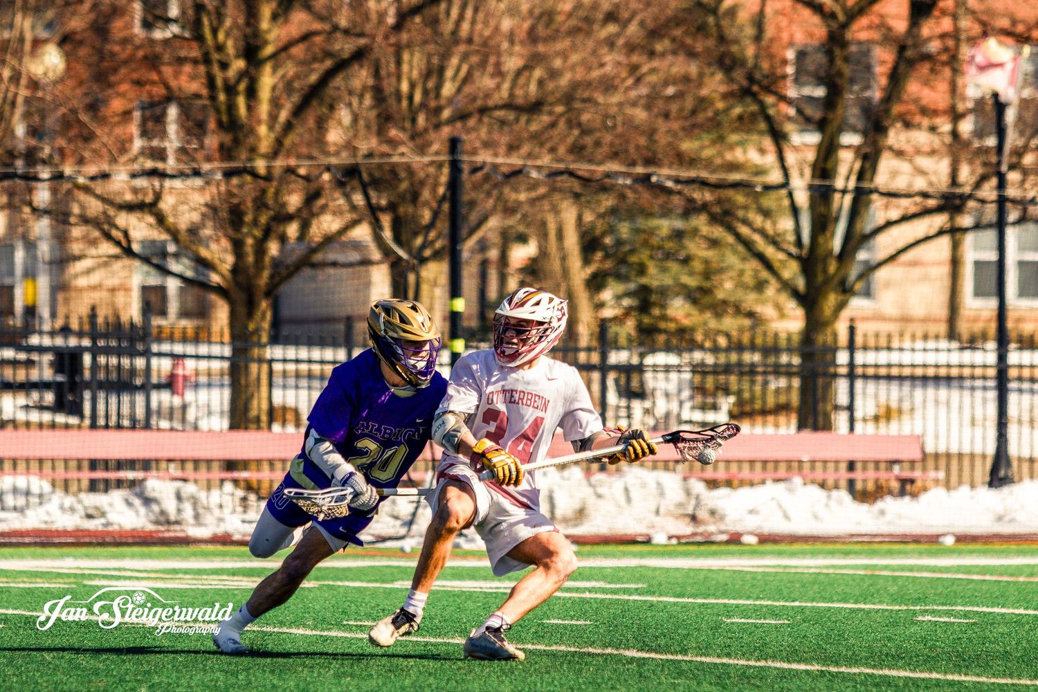 Two lacrosse players battle for position during a competitive match on an artificial turf field.