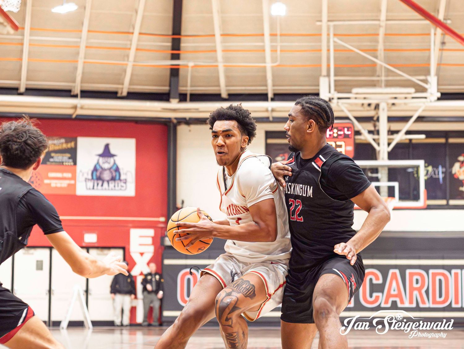 Basketball players compete for possession during an intense college basketball game in a gymnasium.