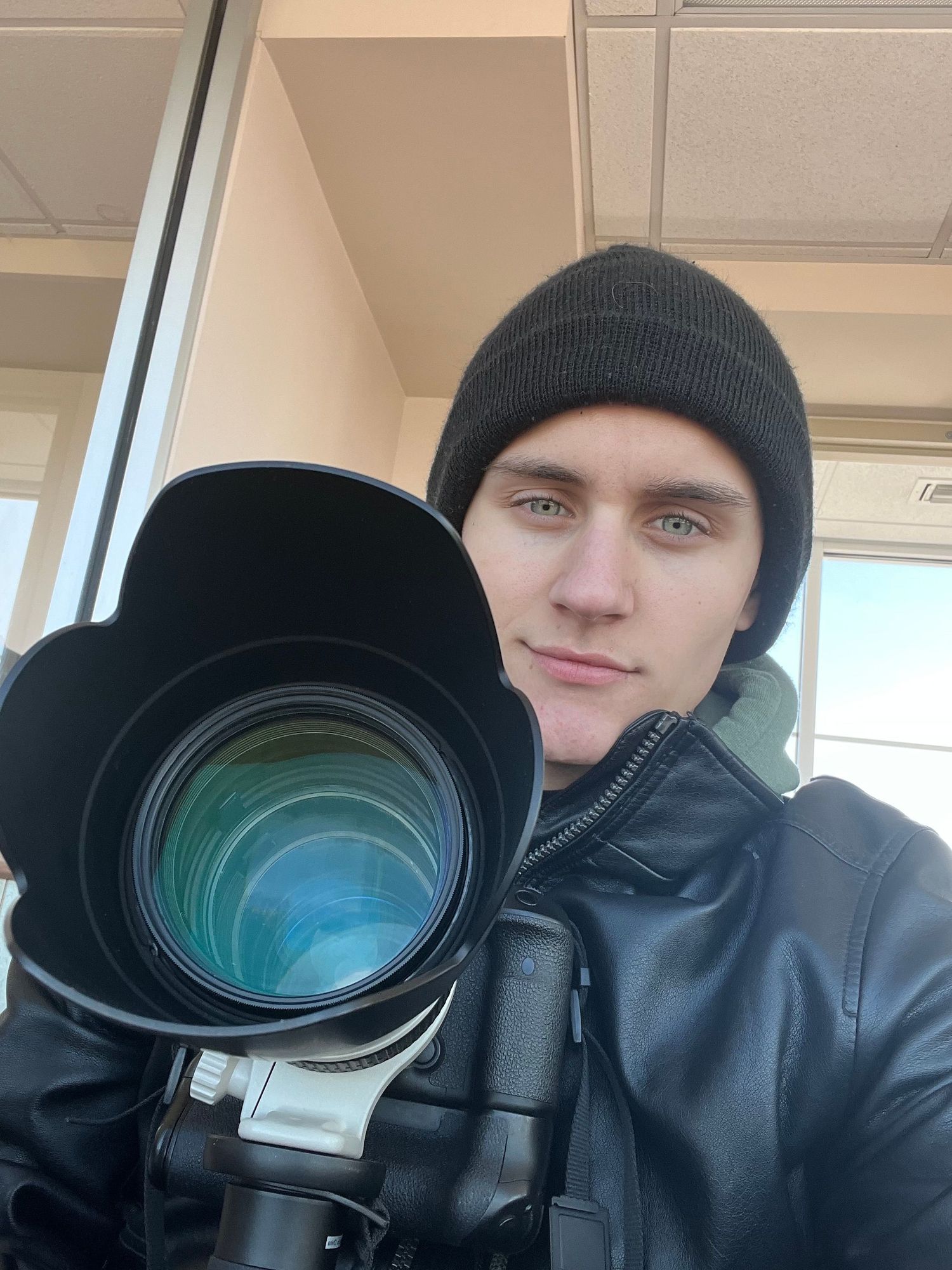 Professional photographer with camera equipment wearing winter beanie and leather jacket on outdoor shoot.