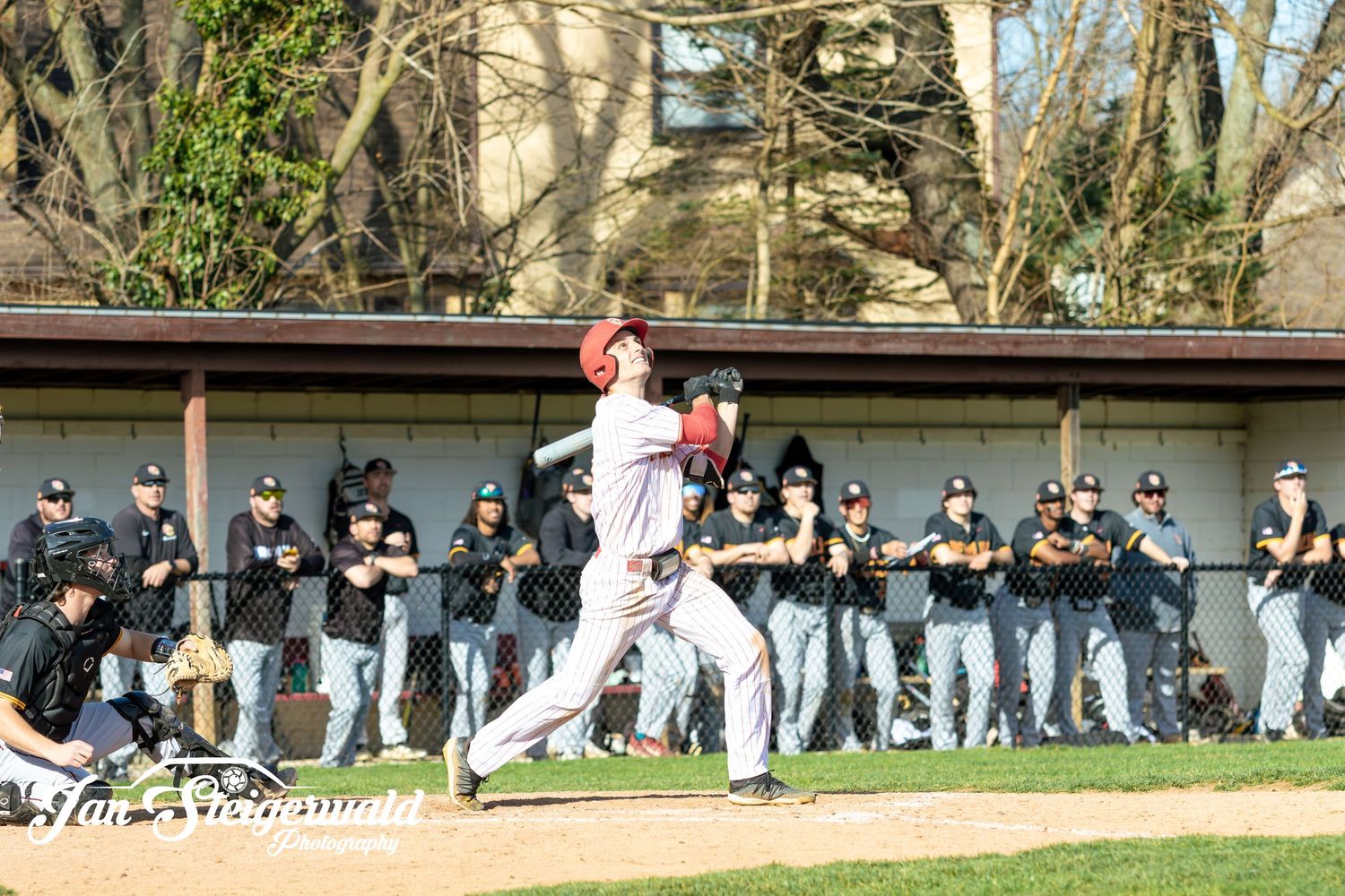 Baseball player swinging a bat on field while team watches from dugout during game.
