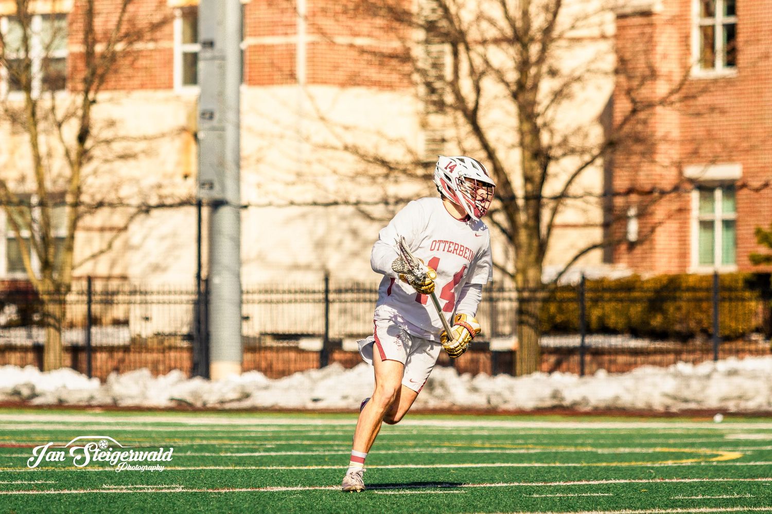 Lacrosse player performs precise follow-through motion on outdoor turf field during afternoon practice session.