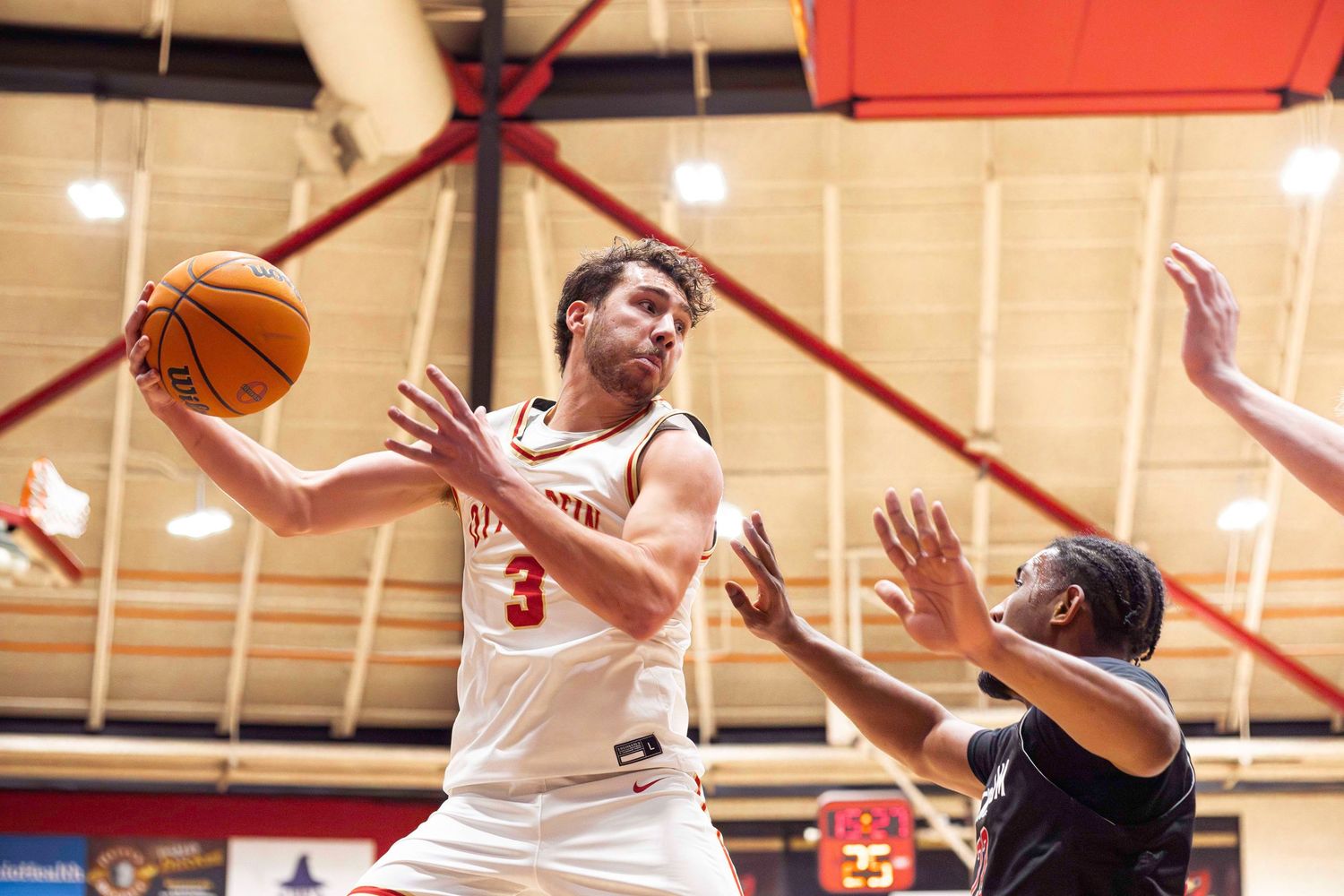 Basketball player in white jersey drives to the basket against defender in indoor gymnasium.