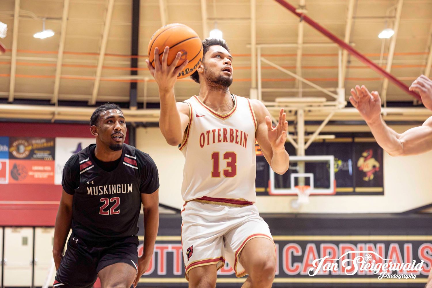 Basketball player in white jersey number 13 drives past defender during competitive game on indoor court.