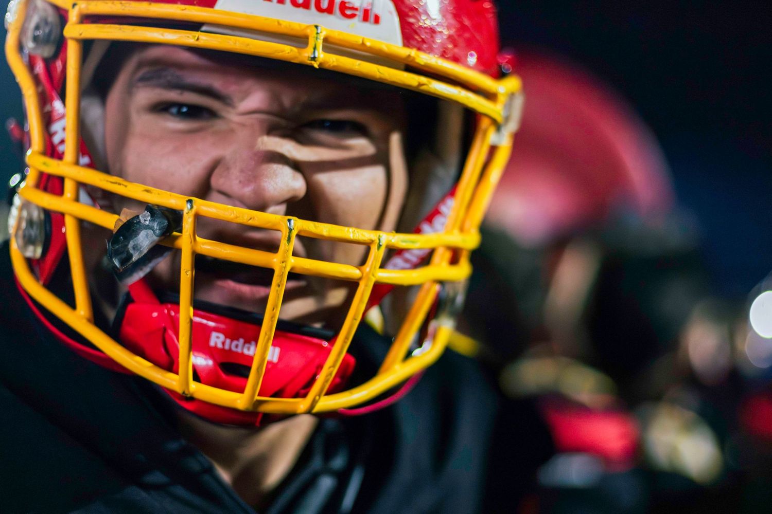 Close-up shot of a football player wearing a red and yellow helmet with protective face mask.