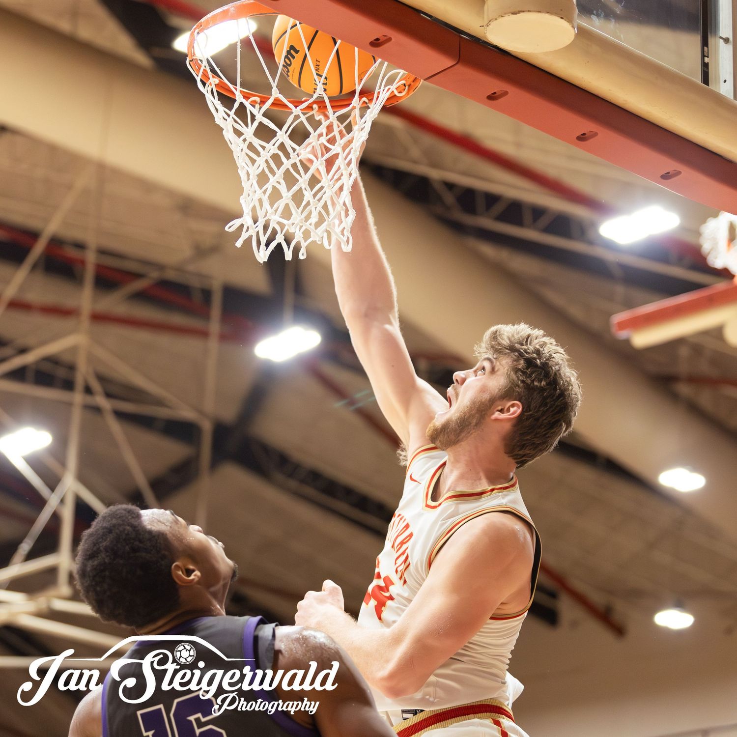 Basketball player reaches up to make a shot near the hoop during a competitive indoor match.