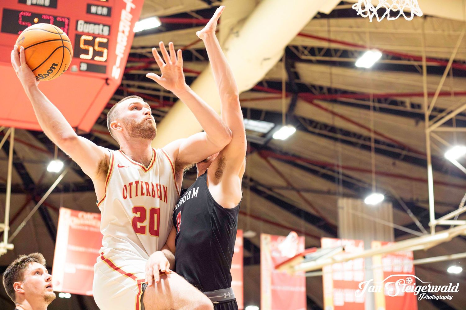 Basketball player in white jersey number 20 leaps for layup against defender during indoor game.