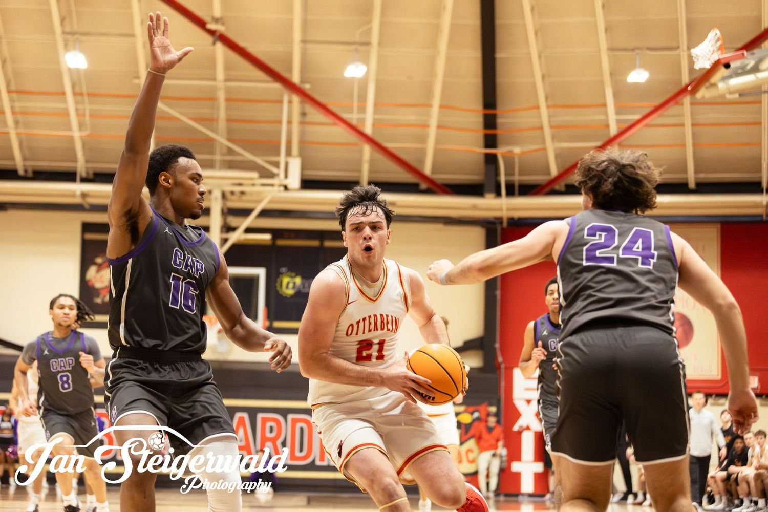 Basketball players compete during an intense indoor game with spectators watching from the sidelines.