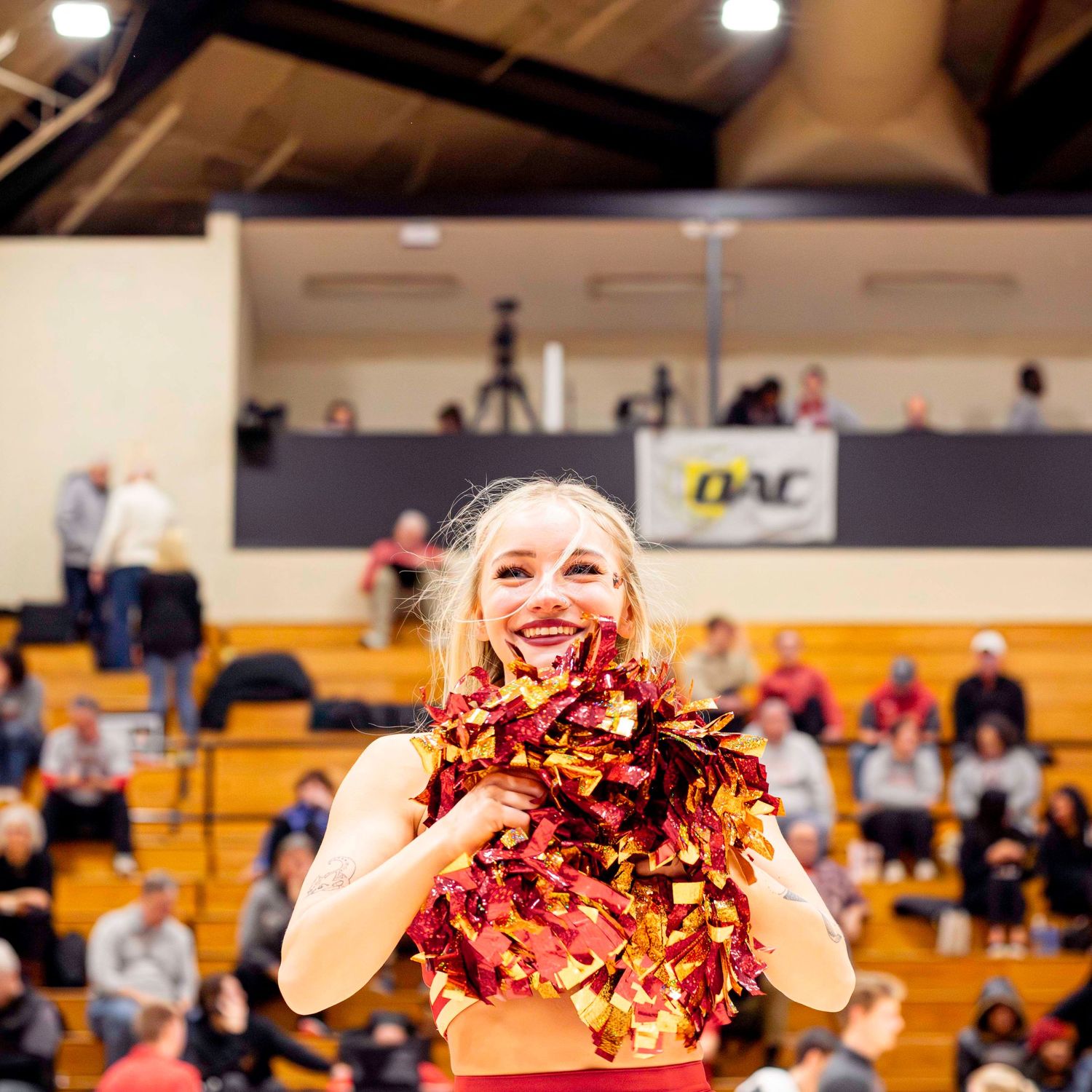 Cheerleader performing with pom poms in gymnasium during indoor event.