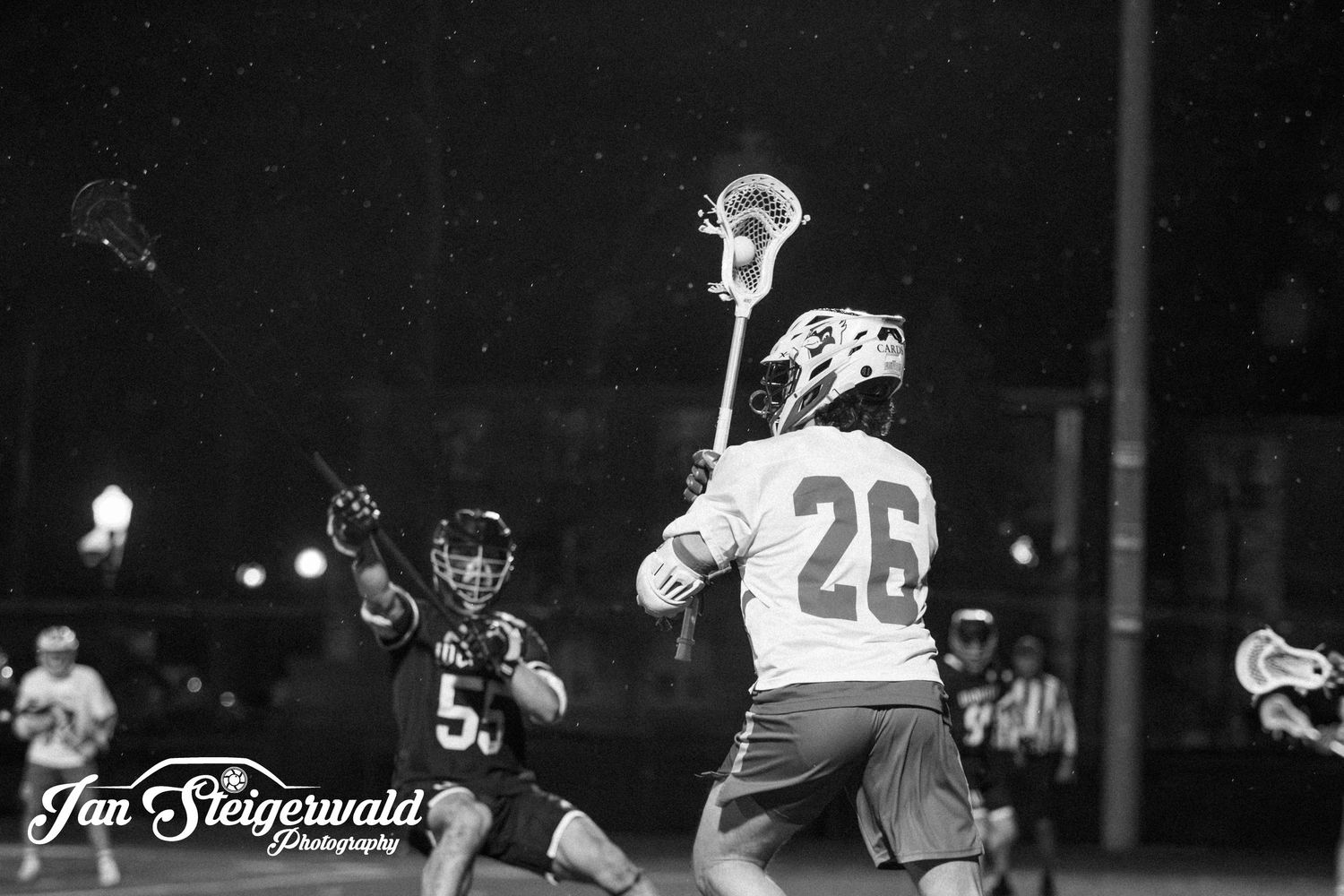 Vintage black and white lacrosse game action photo showing players in motion during a nighttime match.