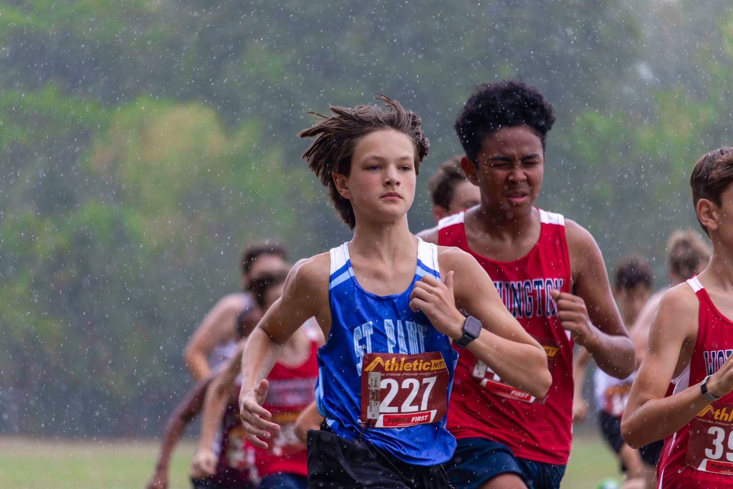 High school cross country runners competing in rainy conditions during race.
