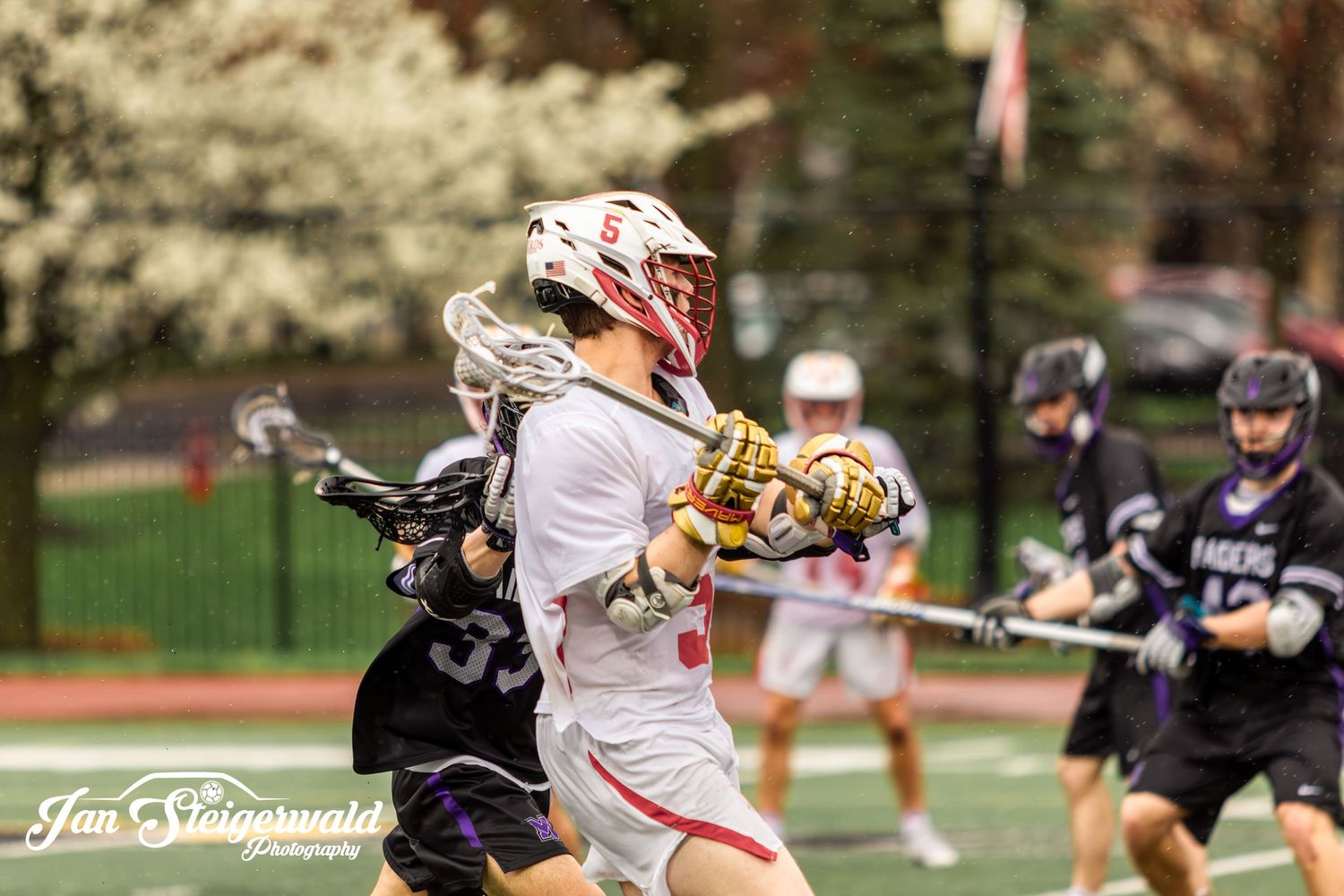 Lacrosse player in white jersey carrying the ball while being defended during an intense game action shot.