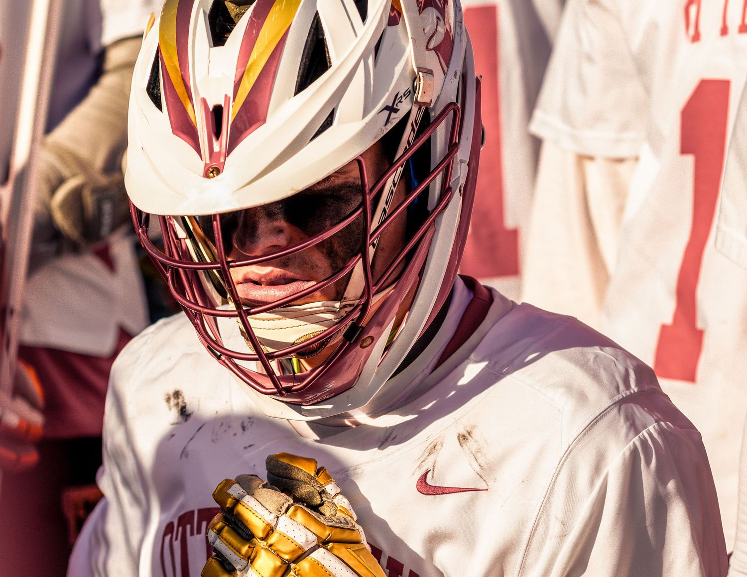 A lacrosse player wearing a white helmet and Nike jersey holds their stick during a game.