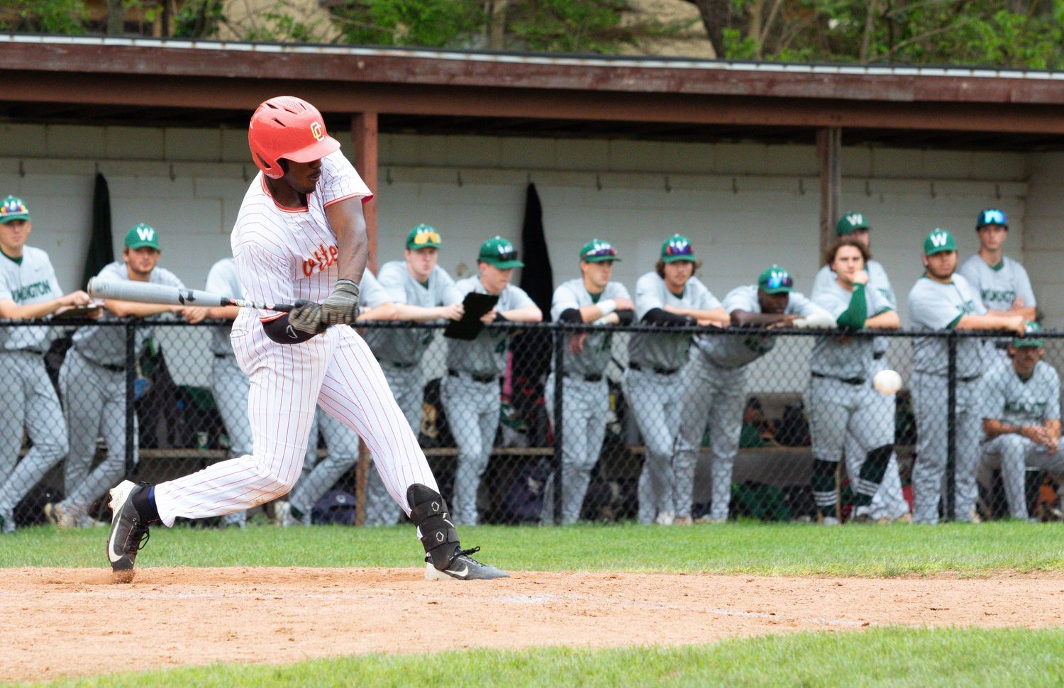 Baseball player in white uniform swinging bat during game with dugout in background.