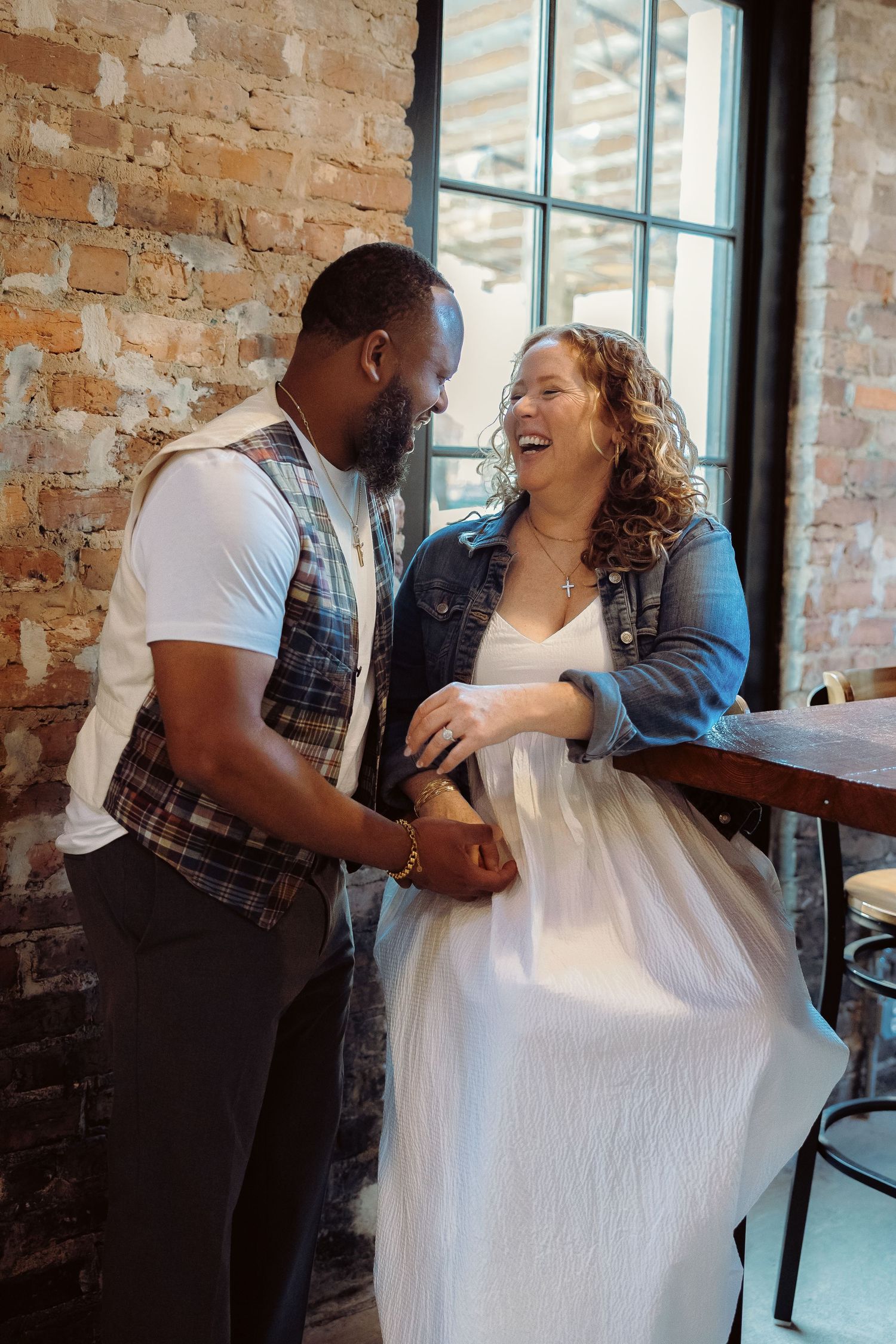 Two people sharing a candid laughing moment together in a rustic brick-walled room.