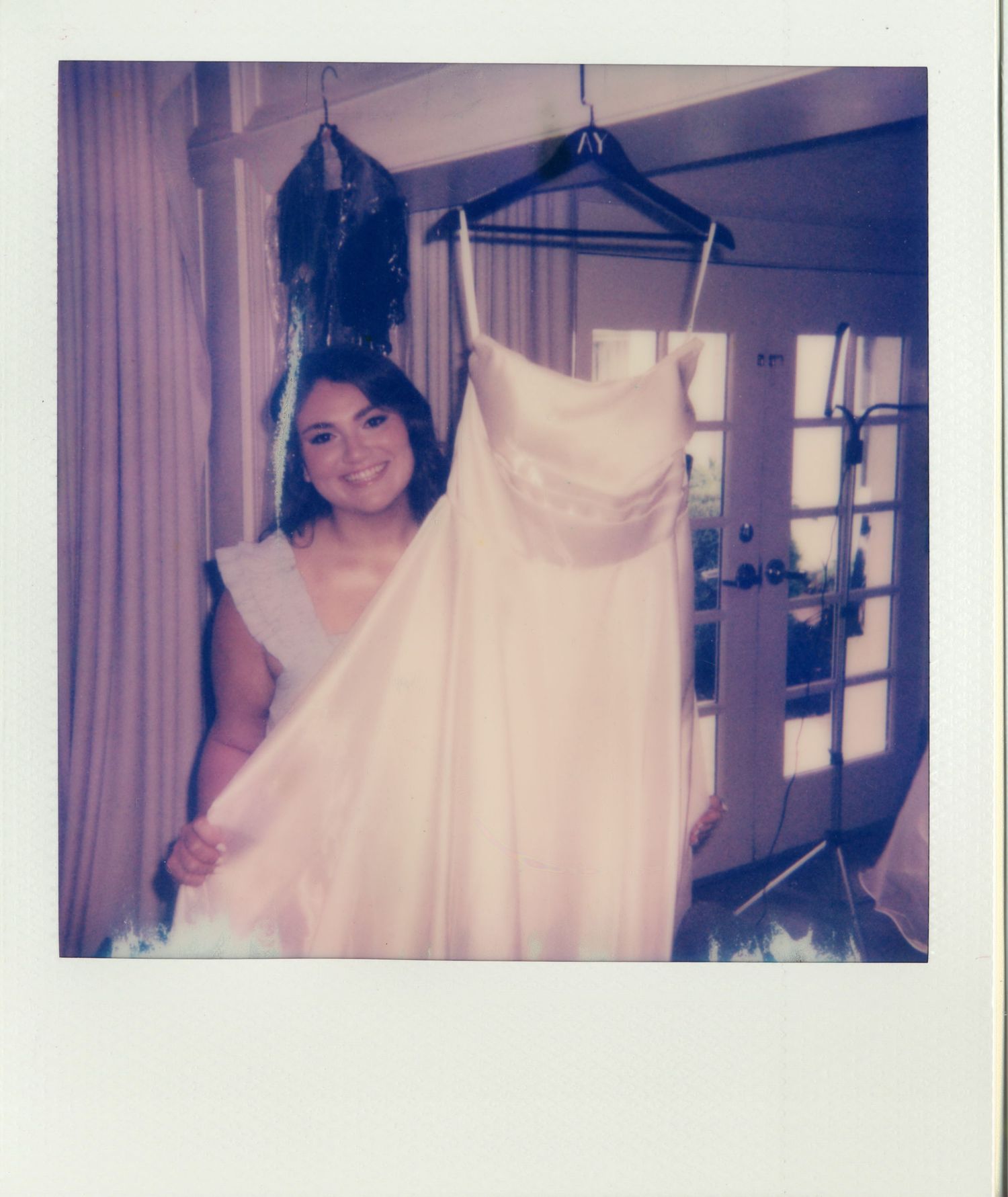 Smiling woman holding a strapless pink wedding gown on a hanger in a bright, elegant room.