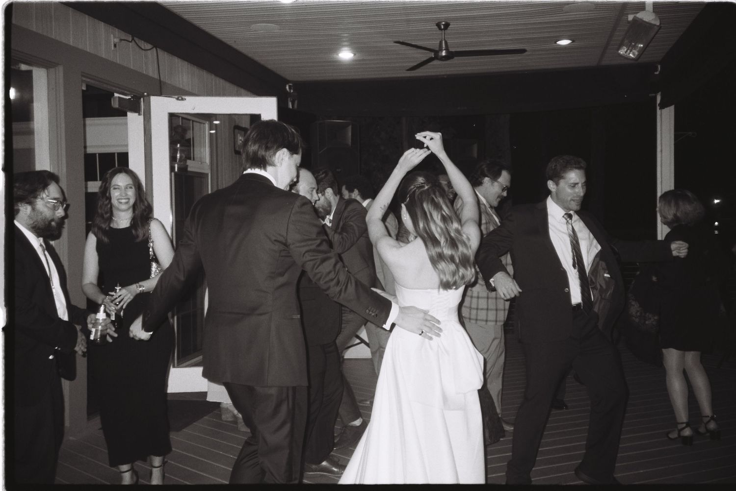 Black and white photo of bride and groom dancing with guests at a wedding reception.