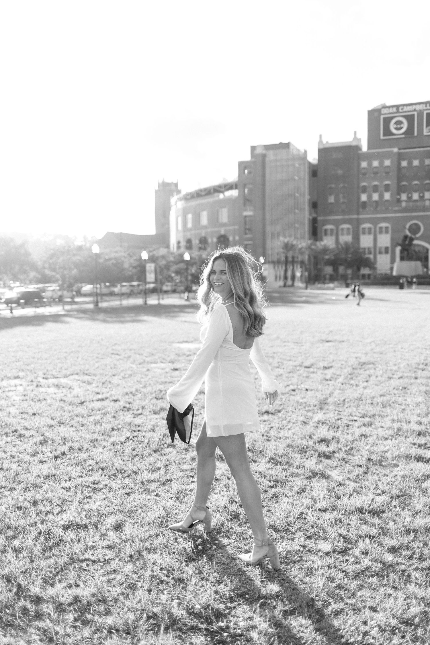 Black and white graduation photos captured on a sunny field with urban backdrop.