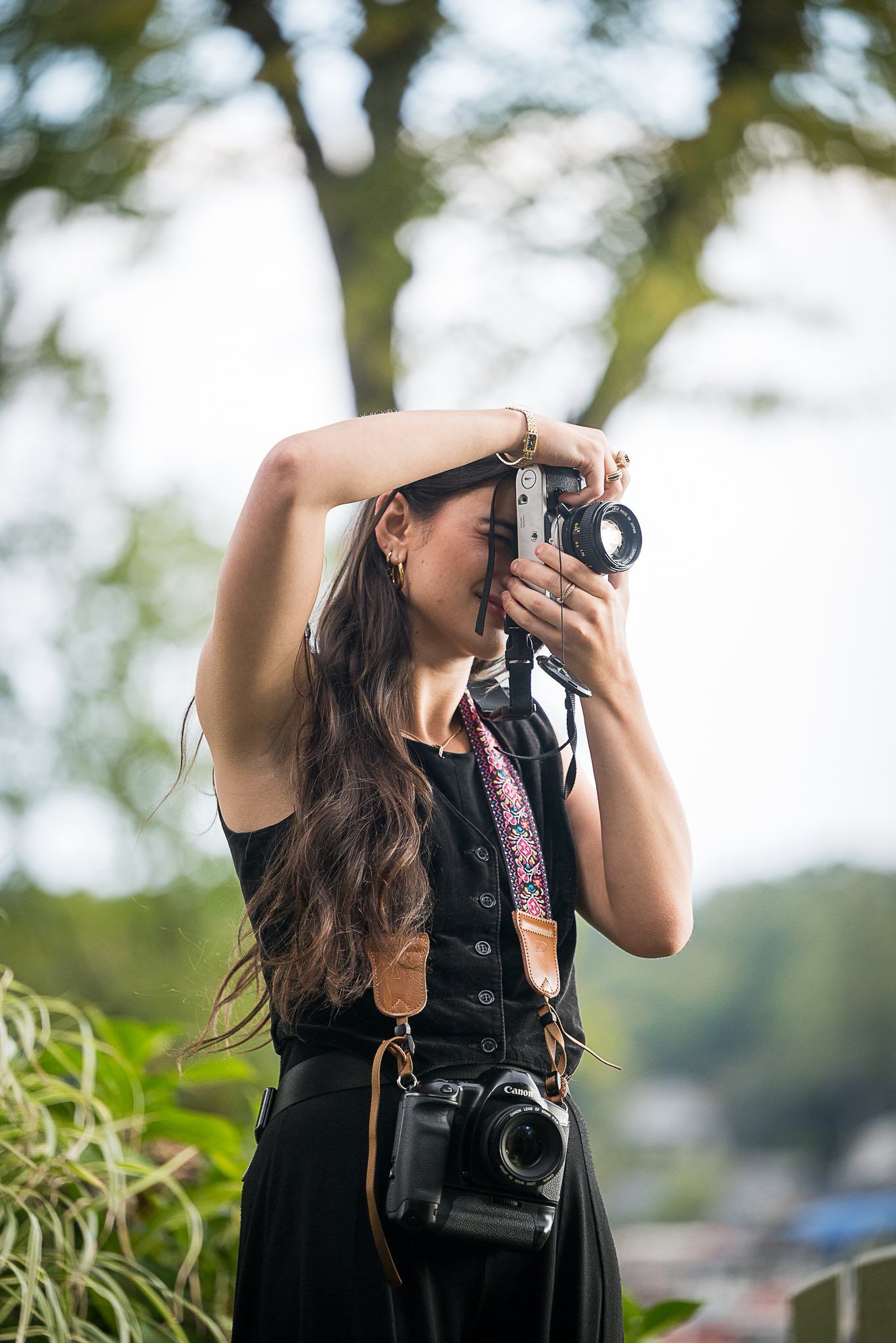 Photographer in black dress takes photos outdoors with professional camera on sunny day.