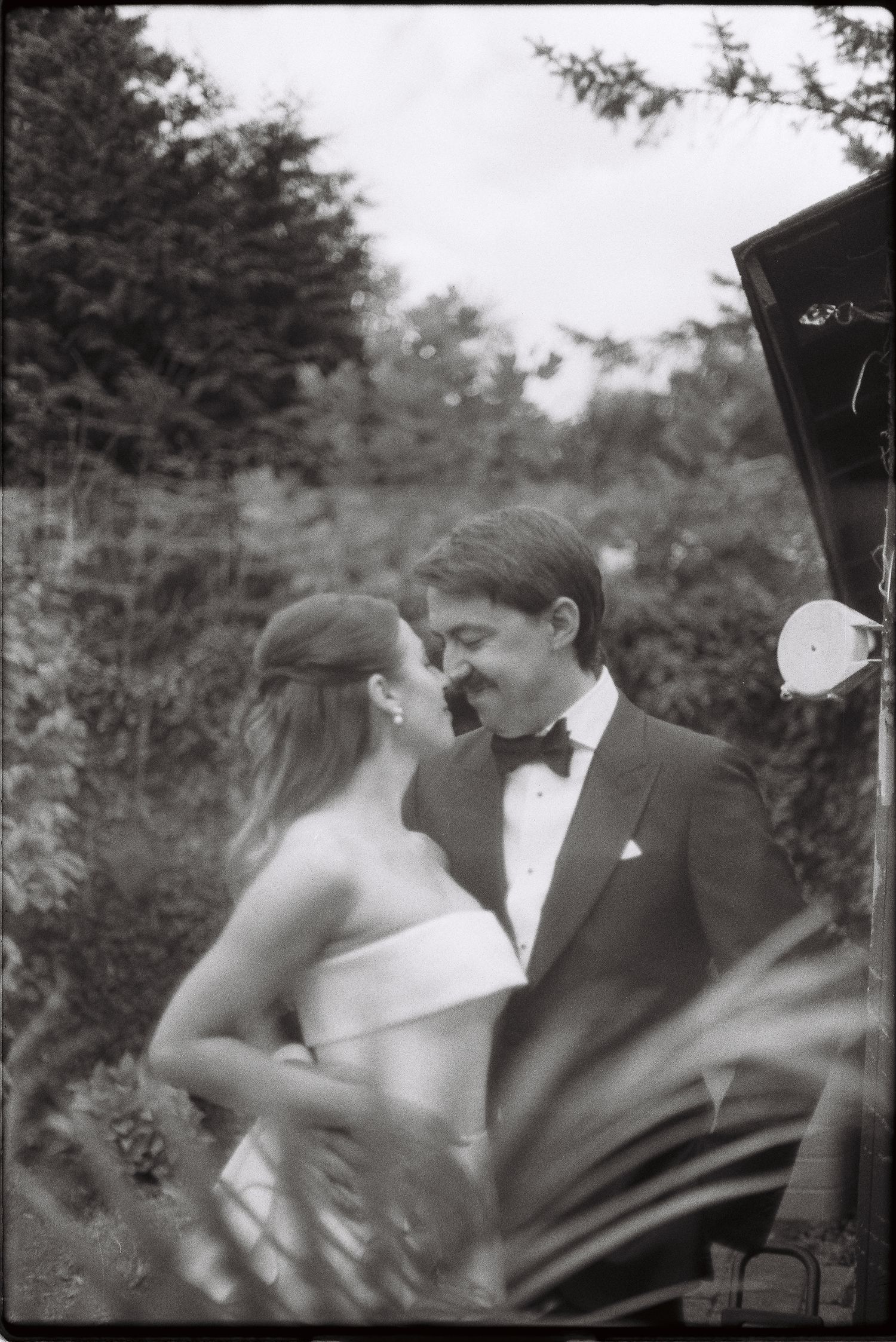 Bride and groom share romantic moment in lush garden in black and white film photo.