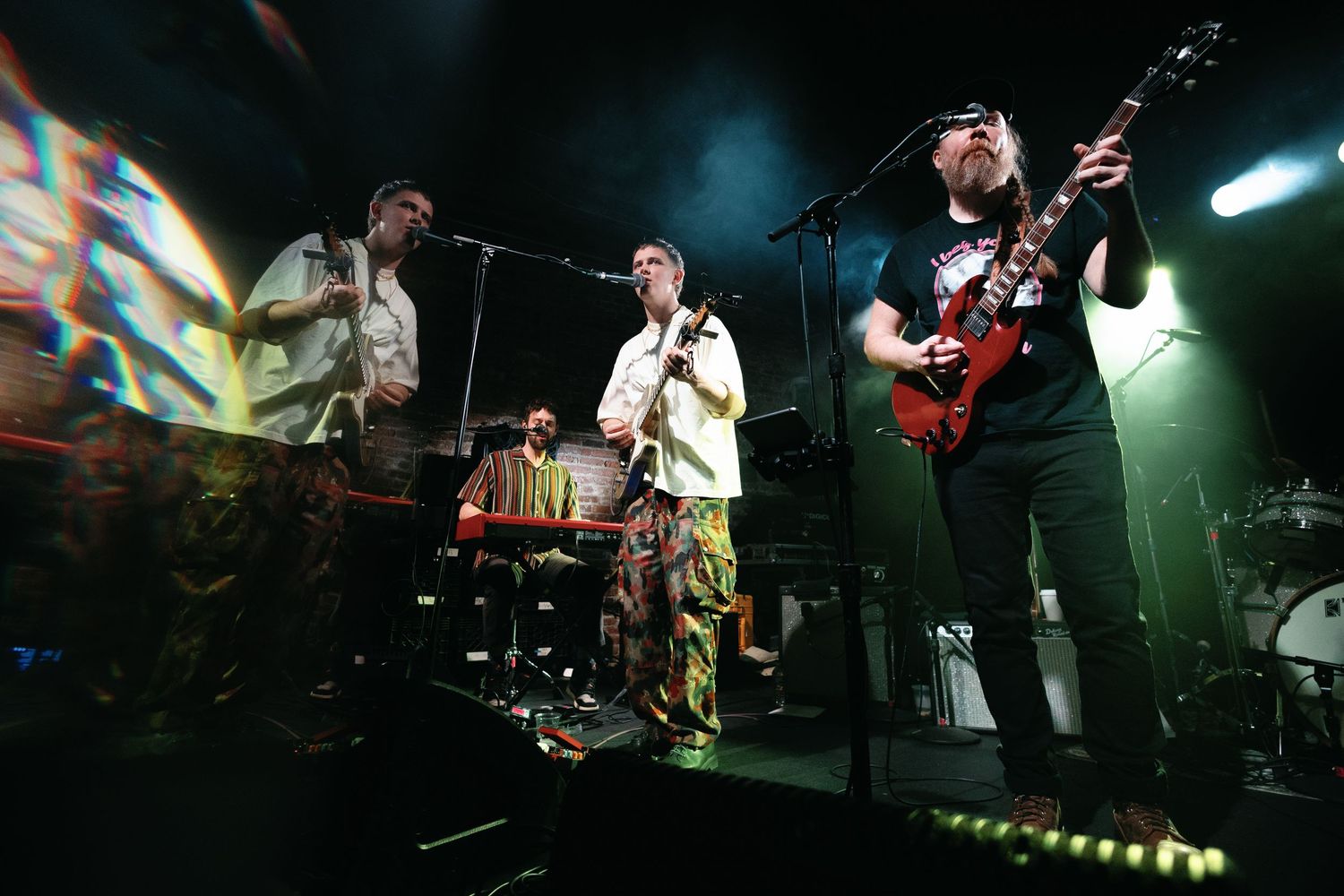 Musicians perform energetically on stage with bright lighting and instruments during a live concert performance.