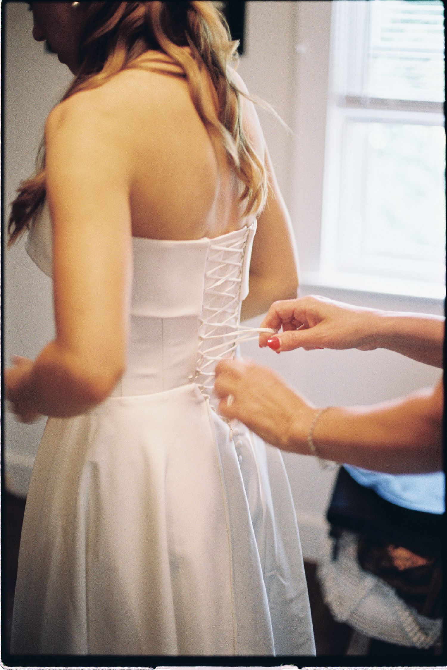 Bridesmaid laces up back of bride's white strapless corset wedding gown.