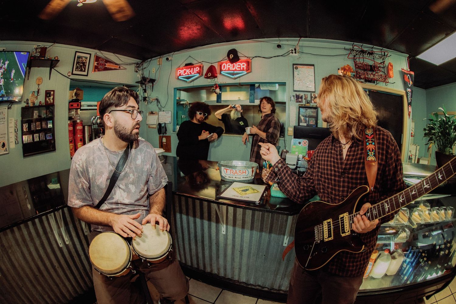 Musicians perform with banjos and instruments in a dimly lit room with pennants and decorations on the wall.