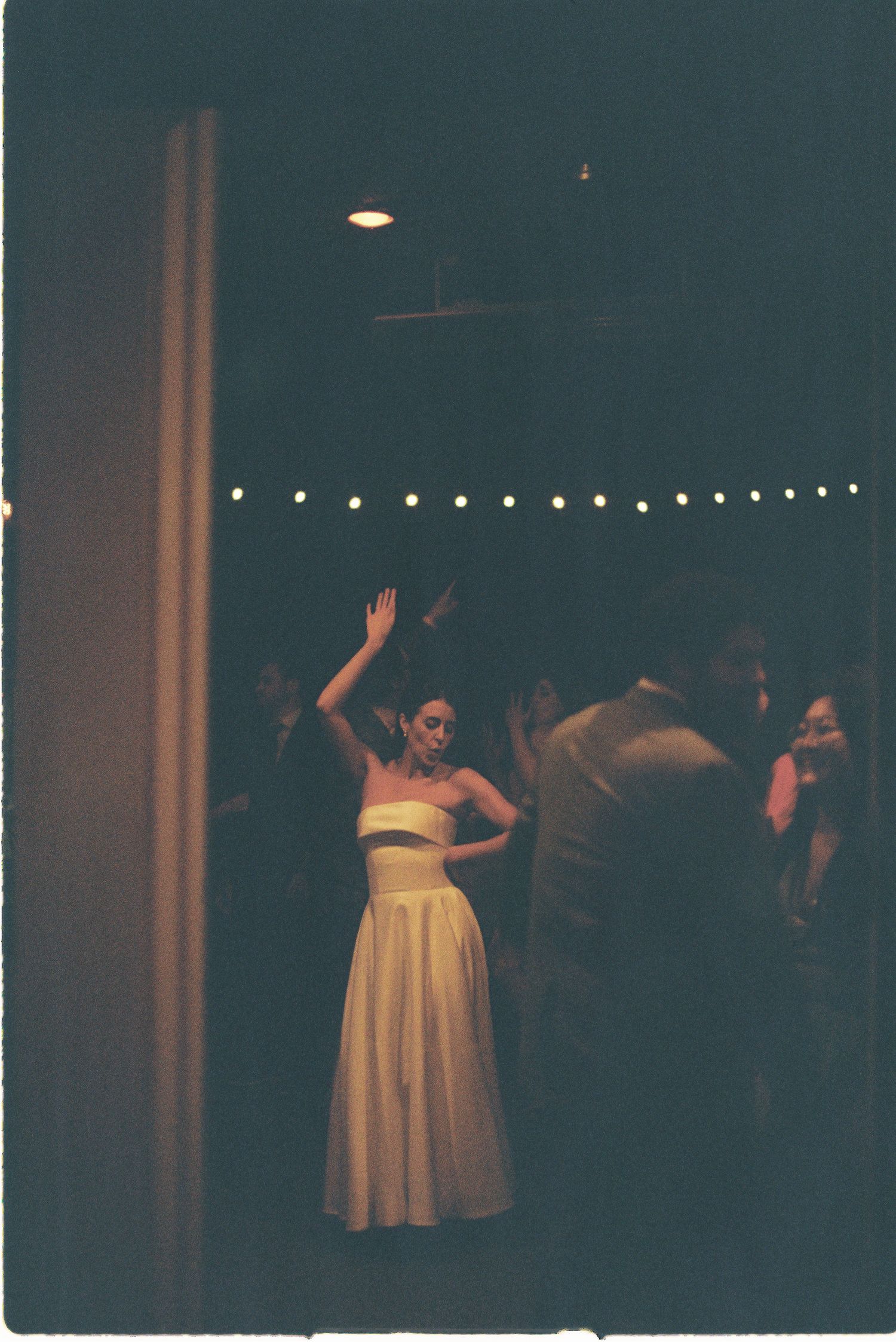 Bride in white strapless gown dancing at elegant wedding reception with string lights.