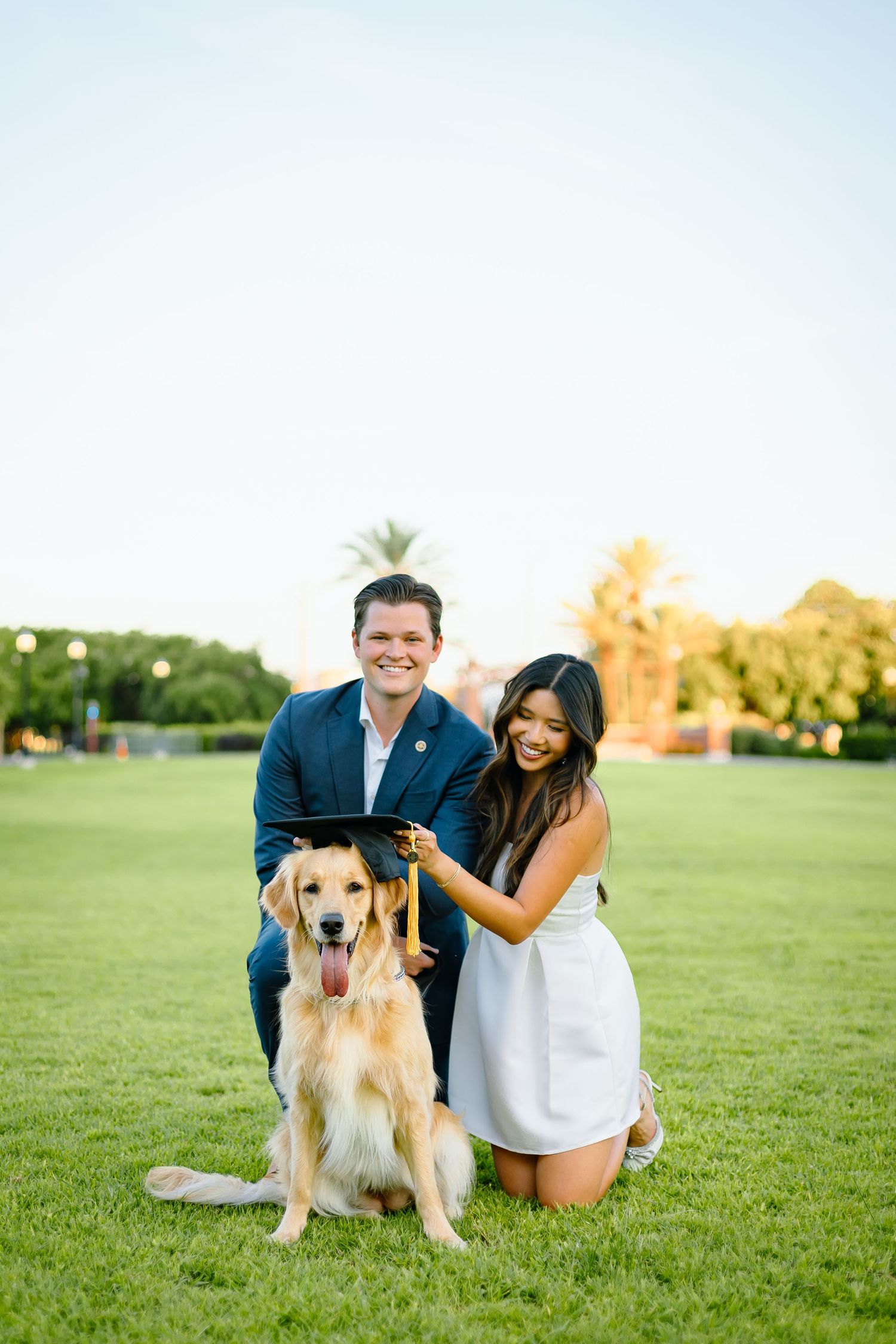 Florida State University Graduate Happy couple poses with their golden retriever on sunny grass field.