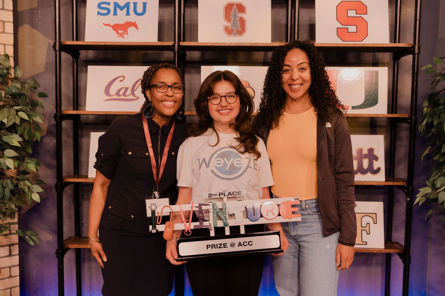 Three people smile together holding an award at an SMU event with display cases in the background.