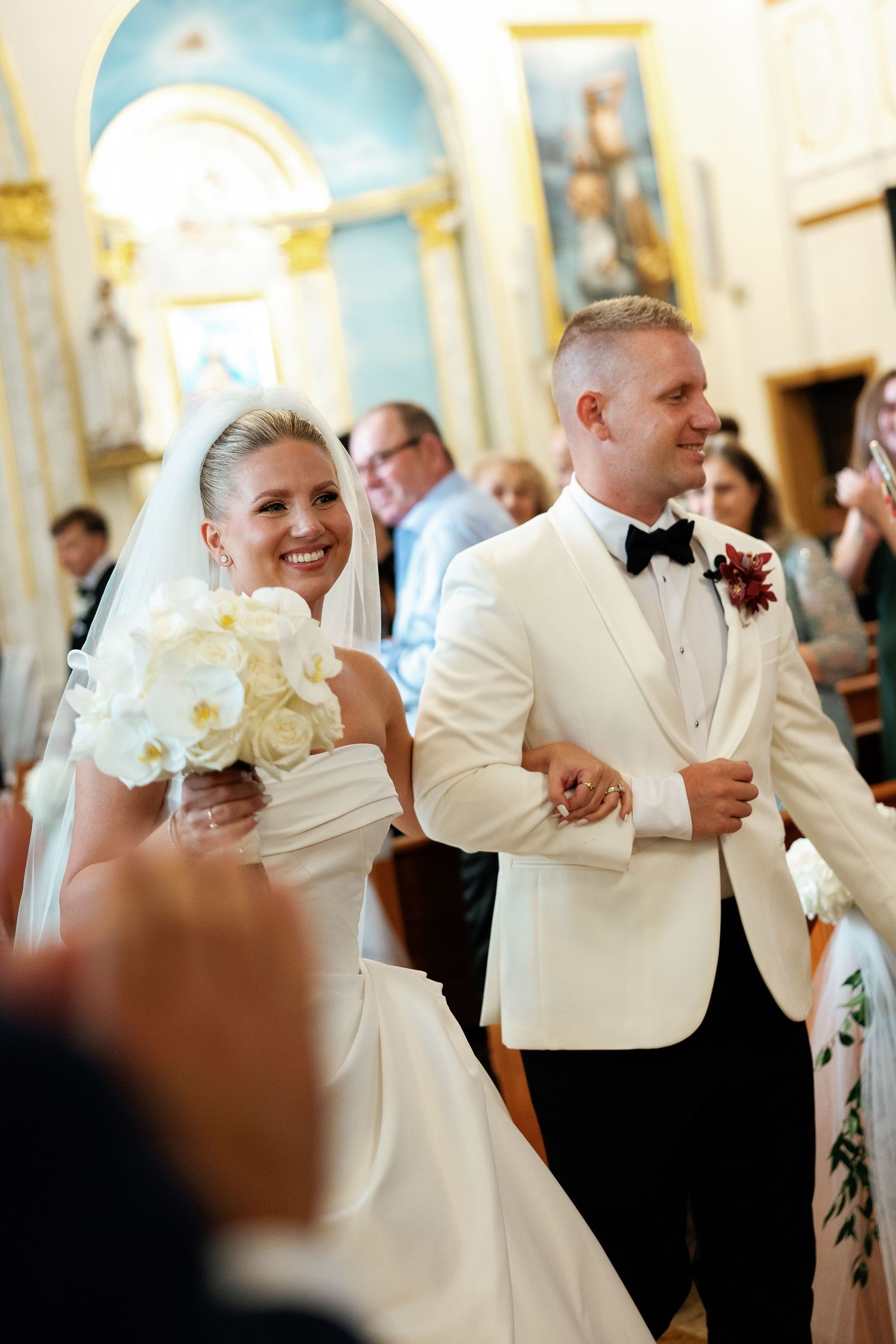 A happy couple shares a joyful dance moment in formal white attire at an elegant indoor venue.
