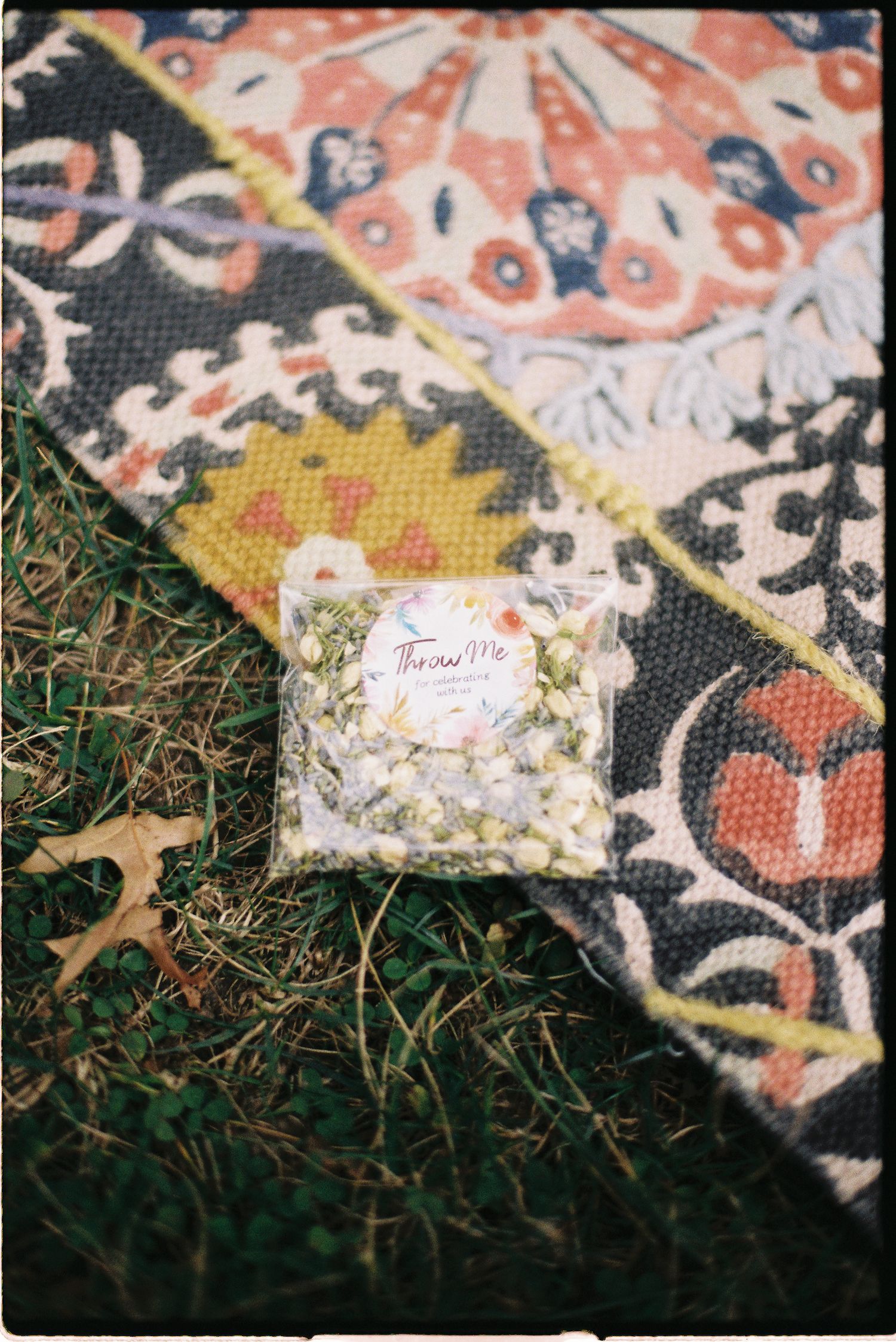 A clear bag of white flower confetti on a colorful floral patterned rug on grass.