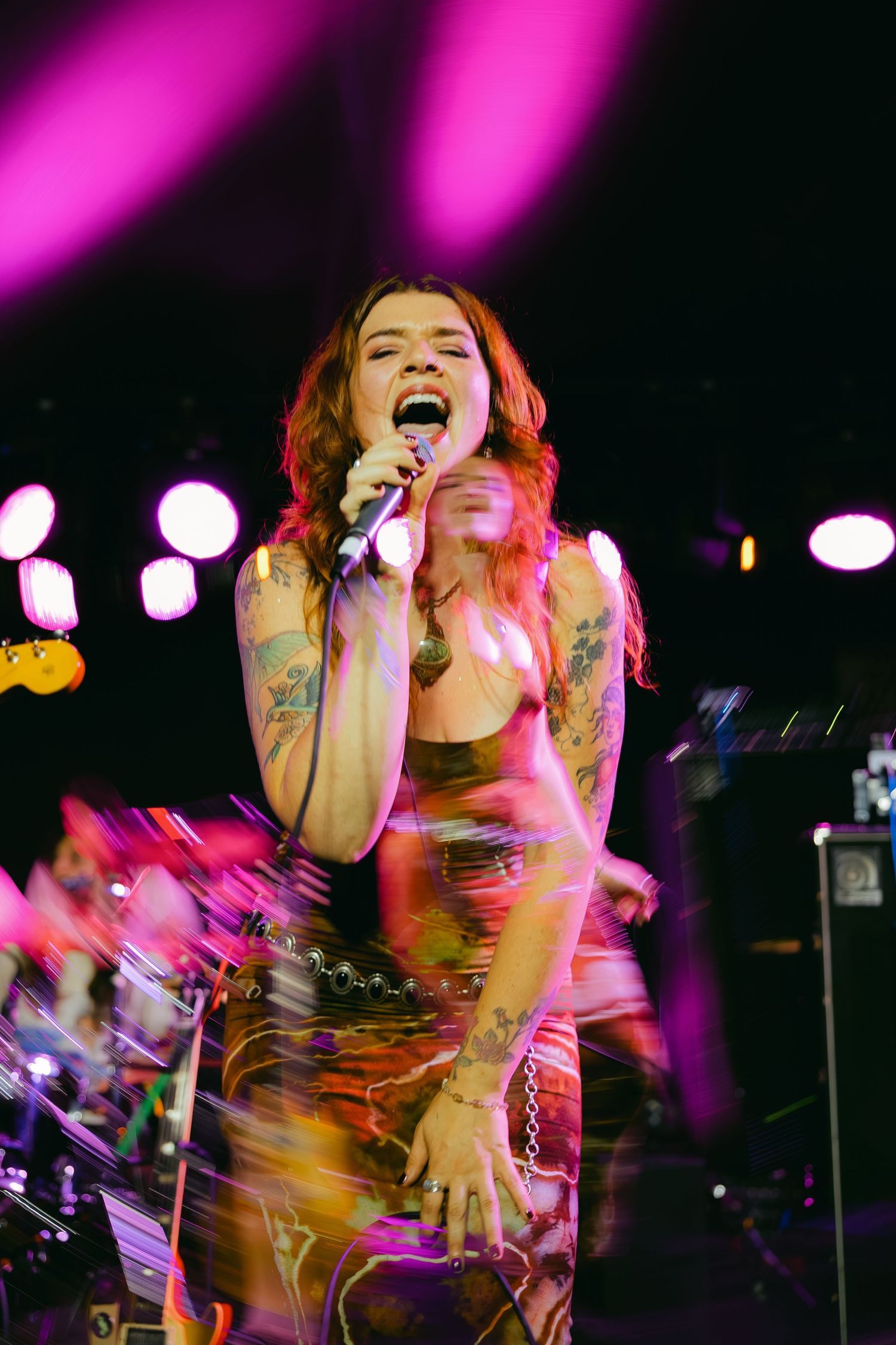 Concert performer in dark venue illuminated by vibrant pink stage lighting creates dynamic motion blur effect during performance.