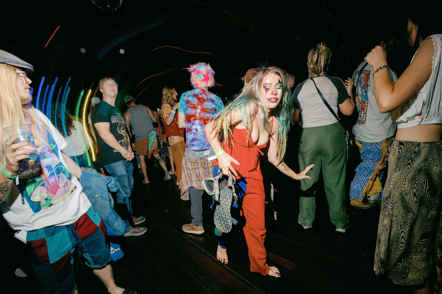 People dancing at a vibrant nightclub party, woman in red jumpsuit dancing on the dance floor.