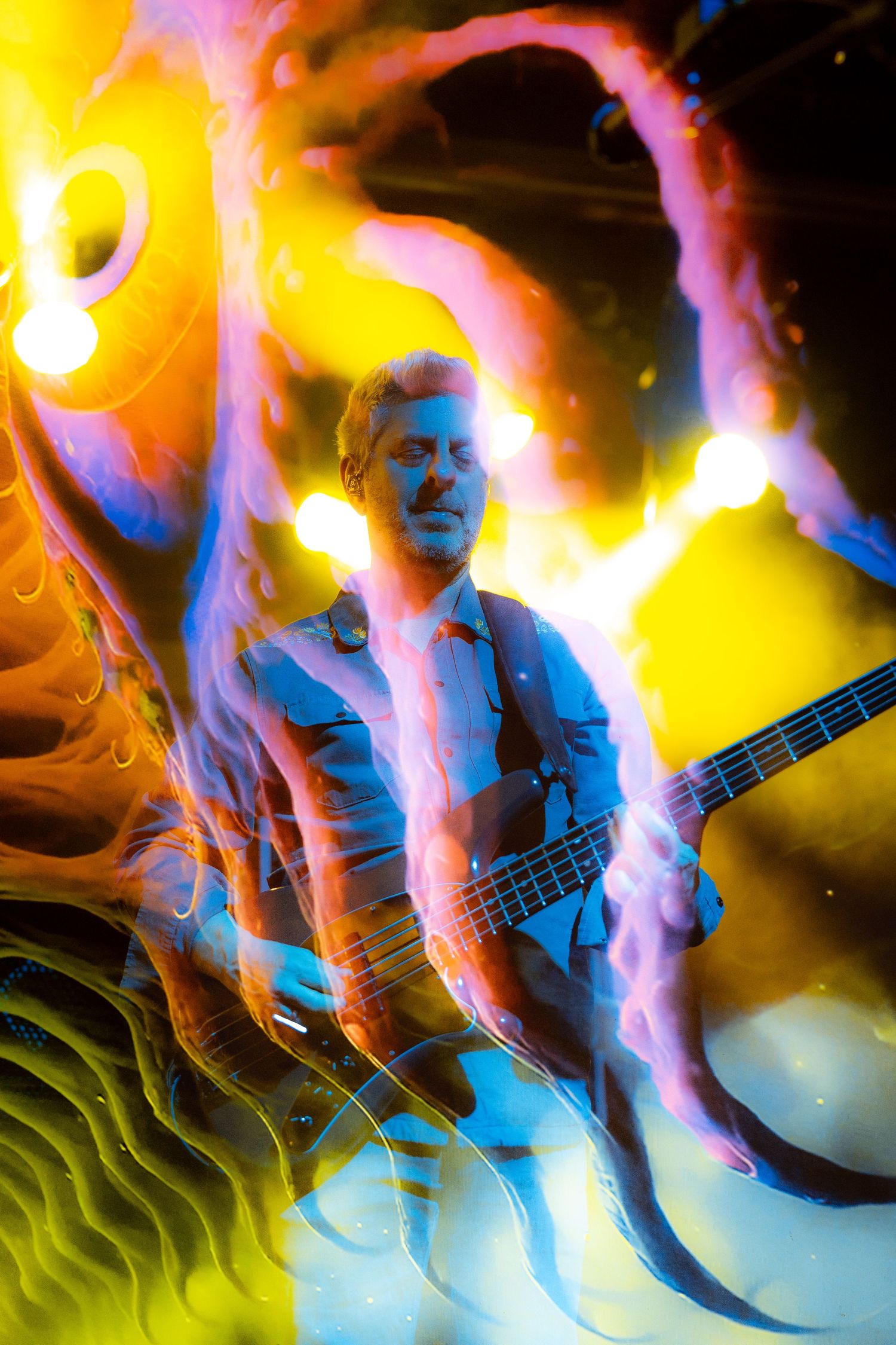 Abstract light painting photograph shows a musician playing bass guitar with colorful yellow and blue light trails.