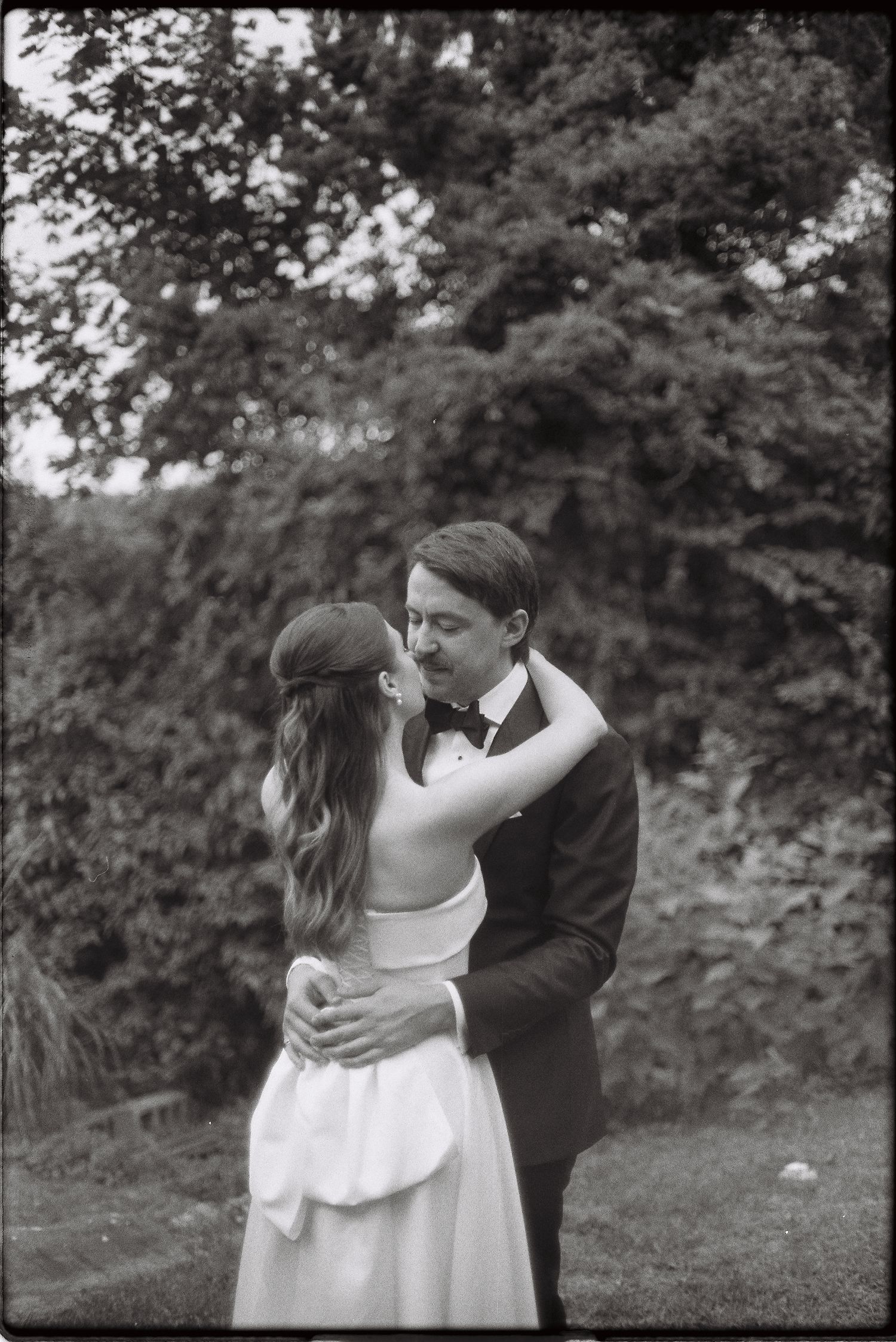 Bride and groom share a tender embrace outdoors in a black and white wedding portrait.