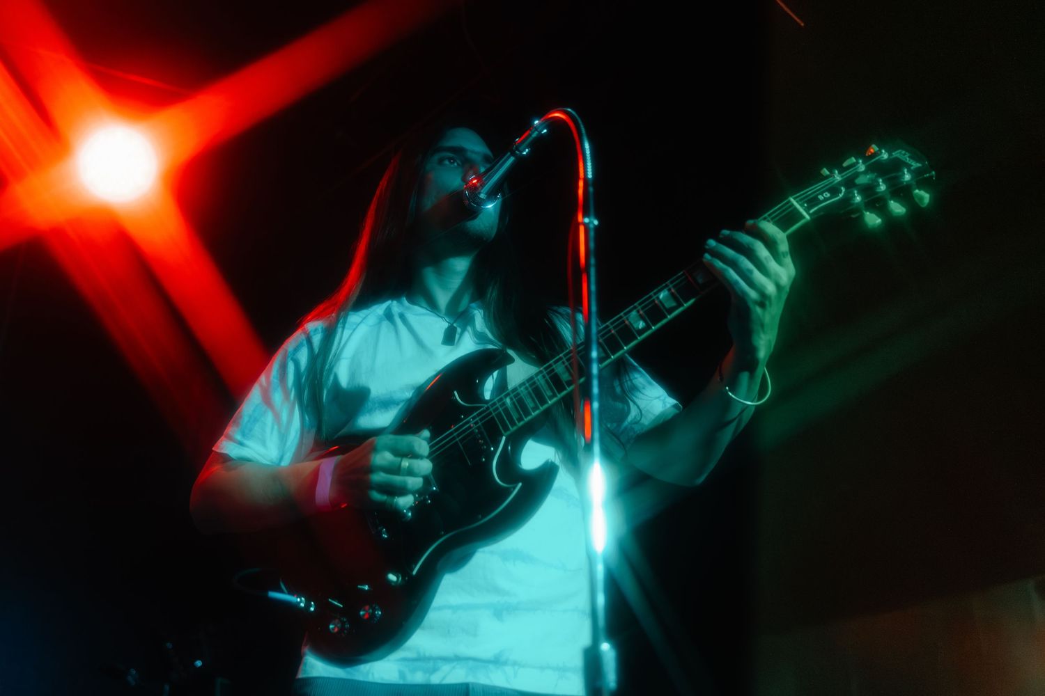 A performer plays guitar and sings on stage under dramatic red and blue lighting effects during a concert performance.