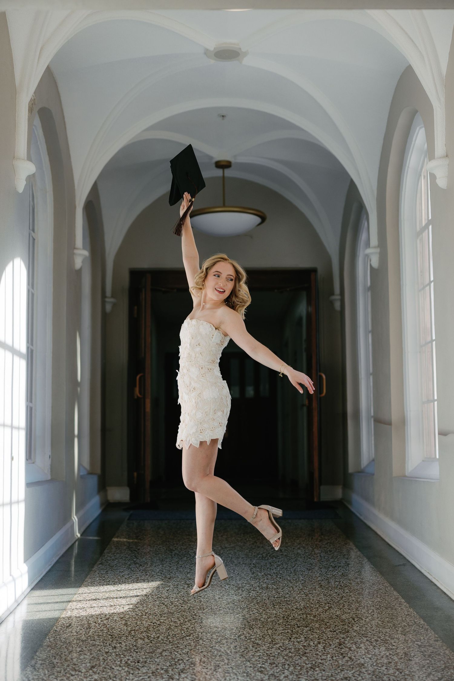 A dancer in white performs graceful leaps and poses in a series of shots along an elegant arched hallway with terrazzo floors.
