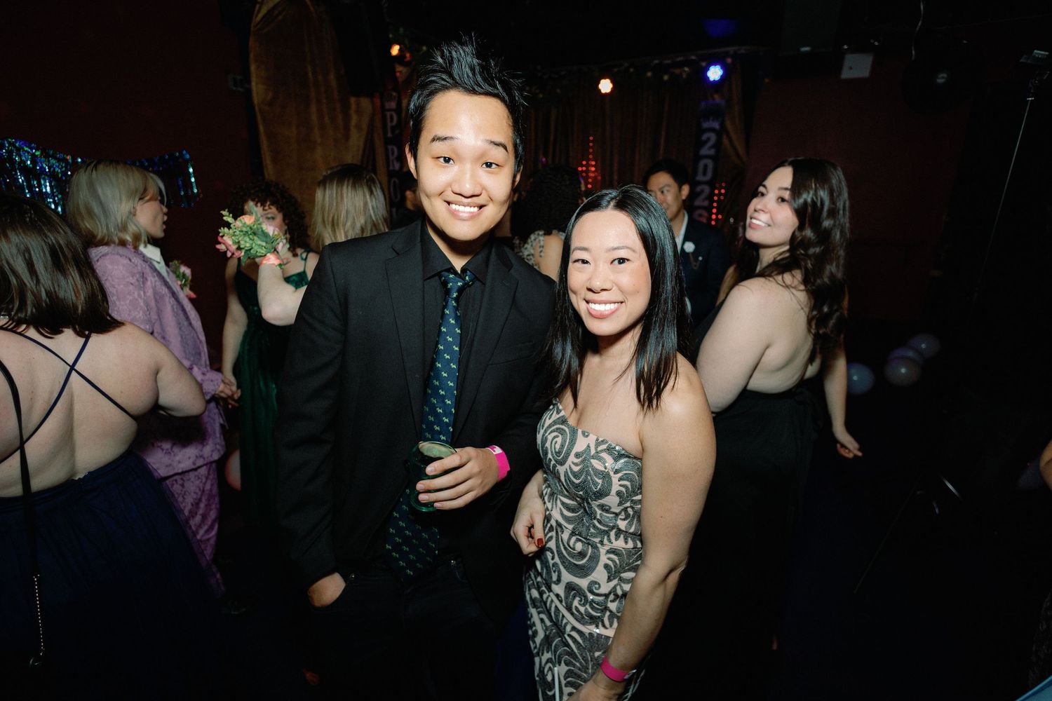 People dancing and socializing at a nightclub or party venue with dark lighting and festive atmosphere.
