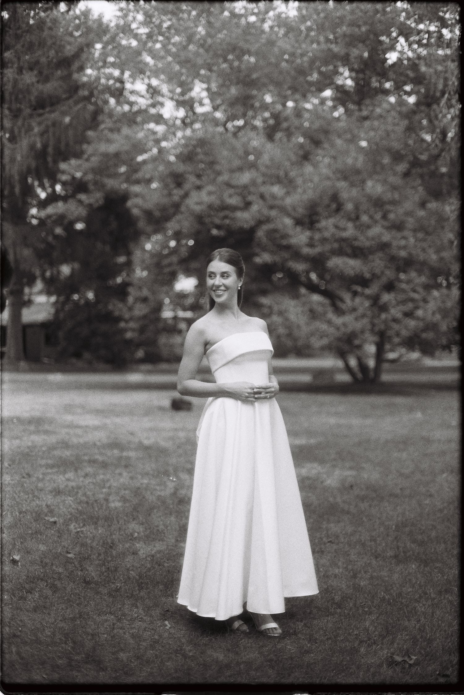 Black and white portrait of smiling bride in strapless gown on green lawn.
