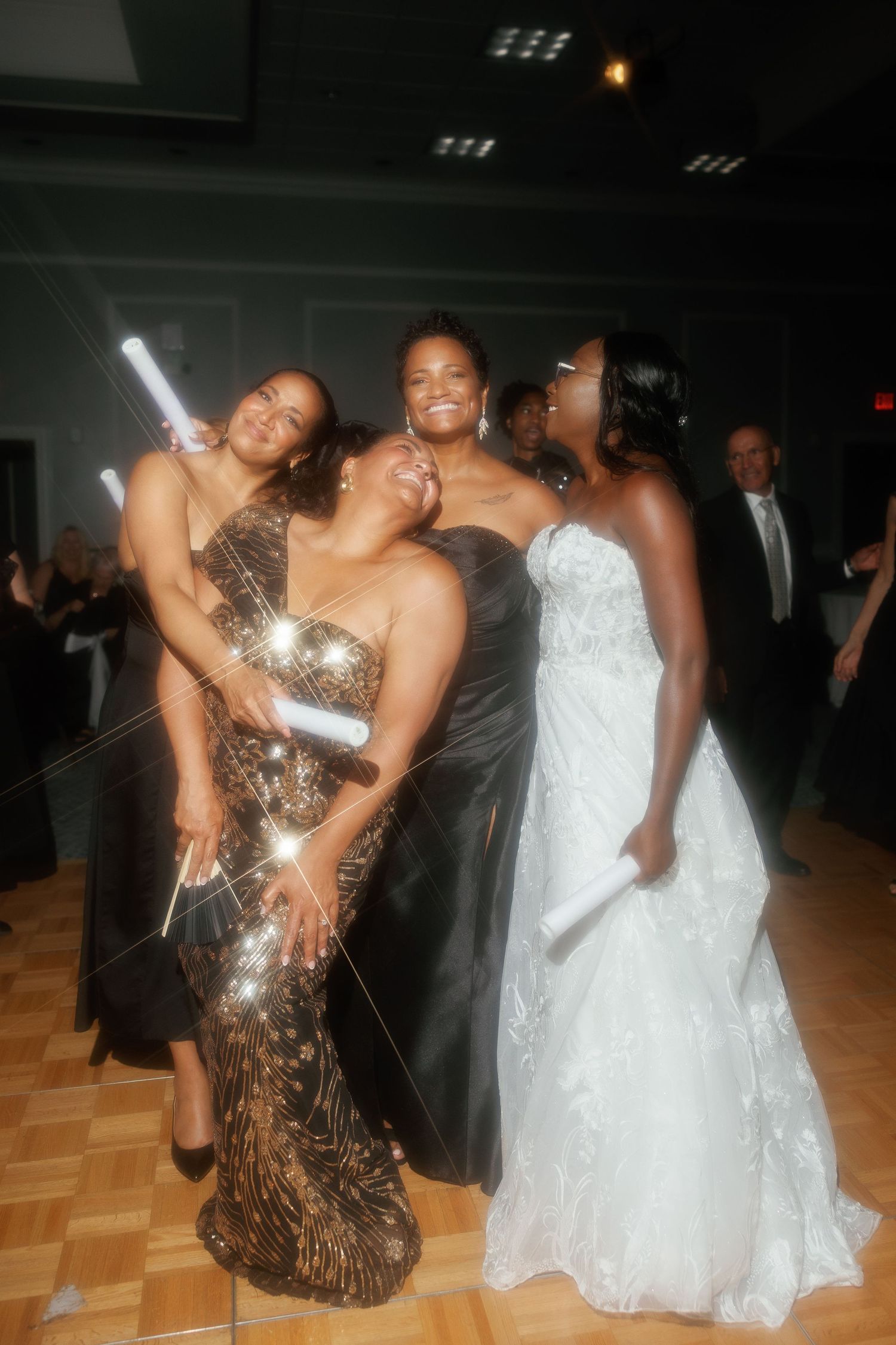 Four women in elegant black and white gowns pose together at a wedding reception.