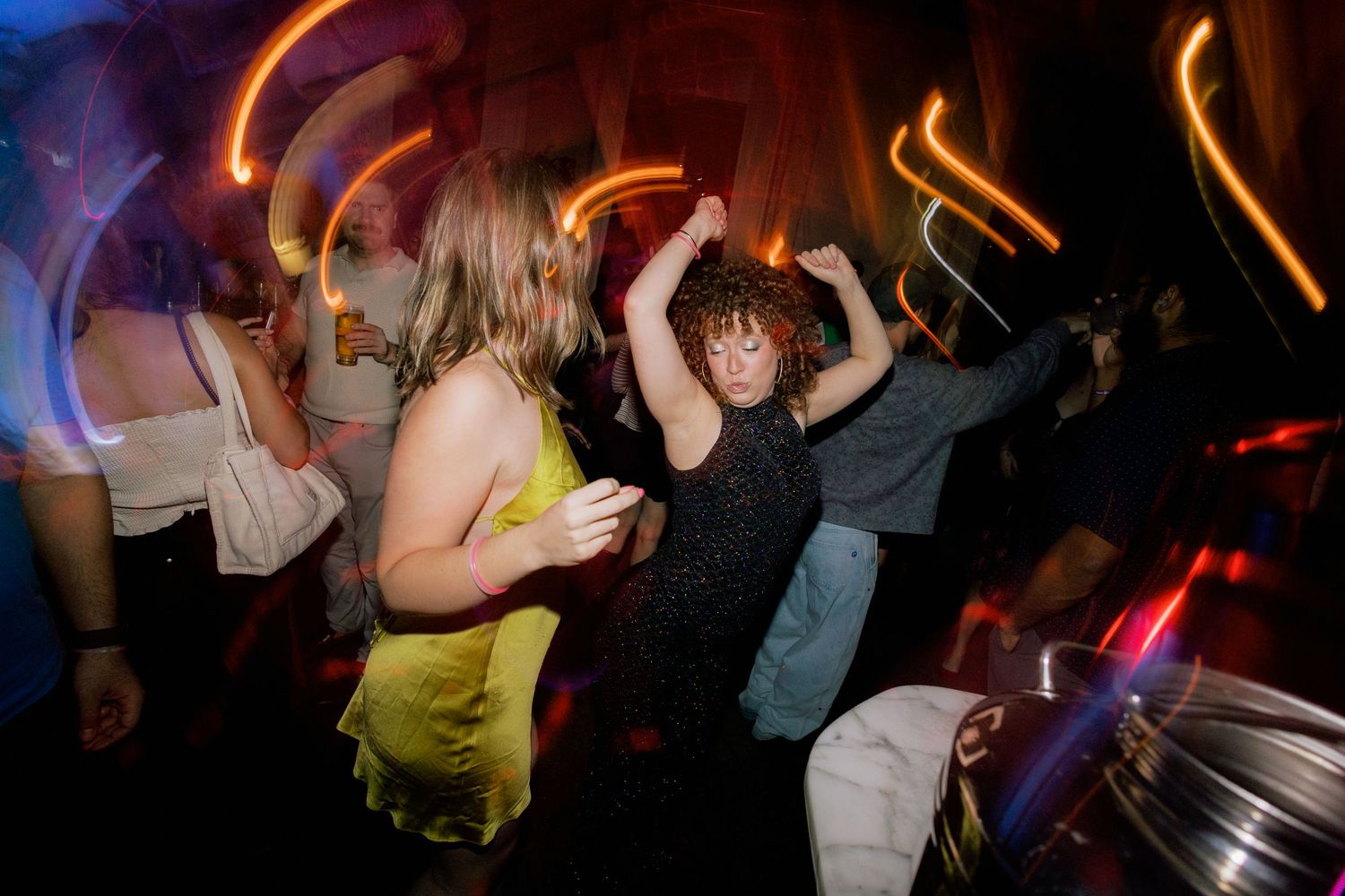 Group of young people dancing energetically at a nightclub with colorful light trails.