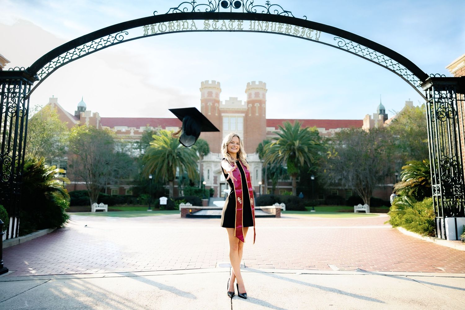A person in a dress walks through a university campus courtyard on a sunny day.