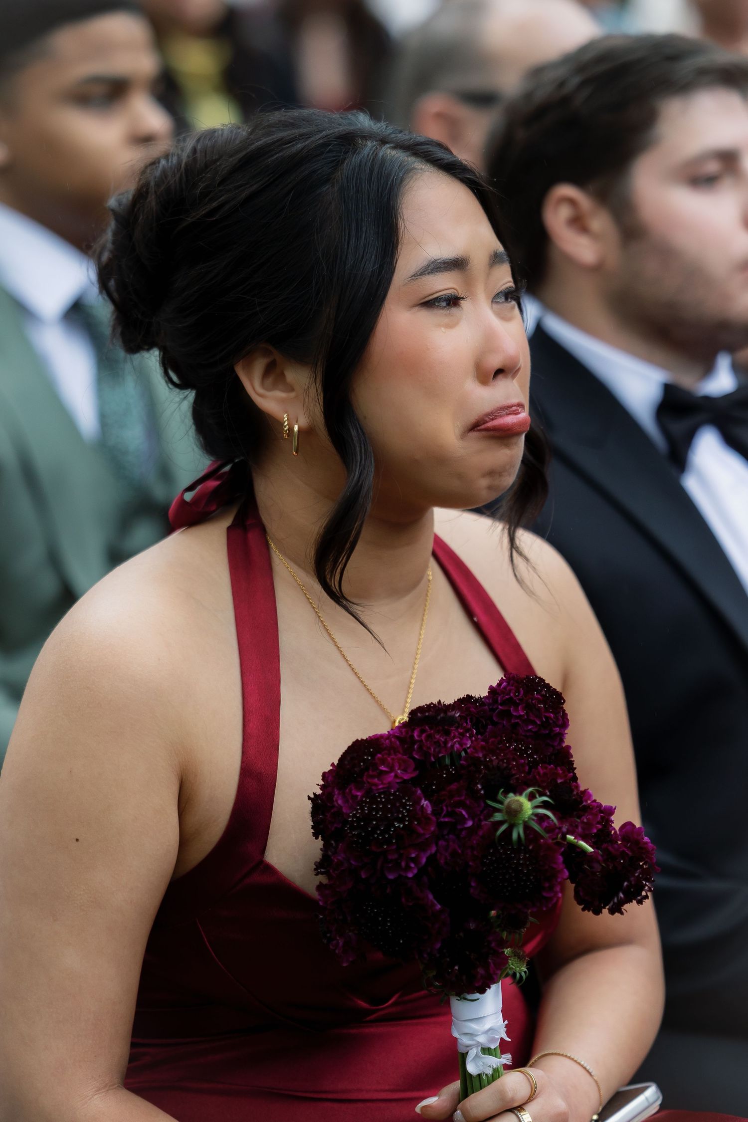 Emotional bridesmaid in red dress crying while holding dark floral bouquet at wedding.