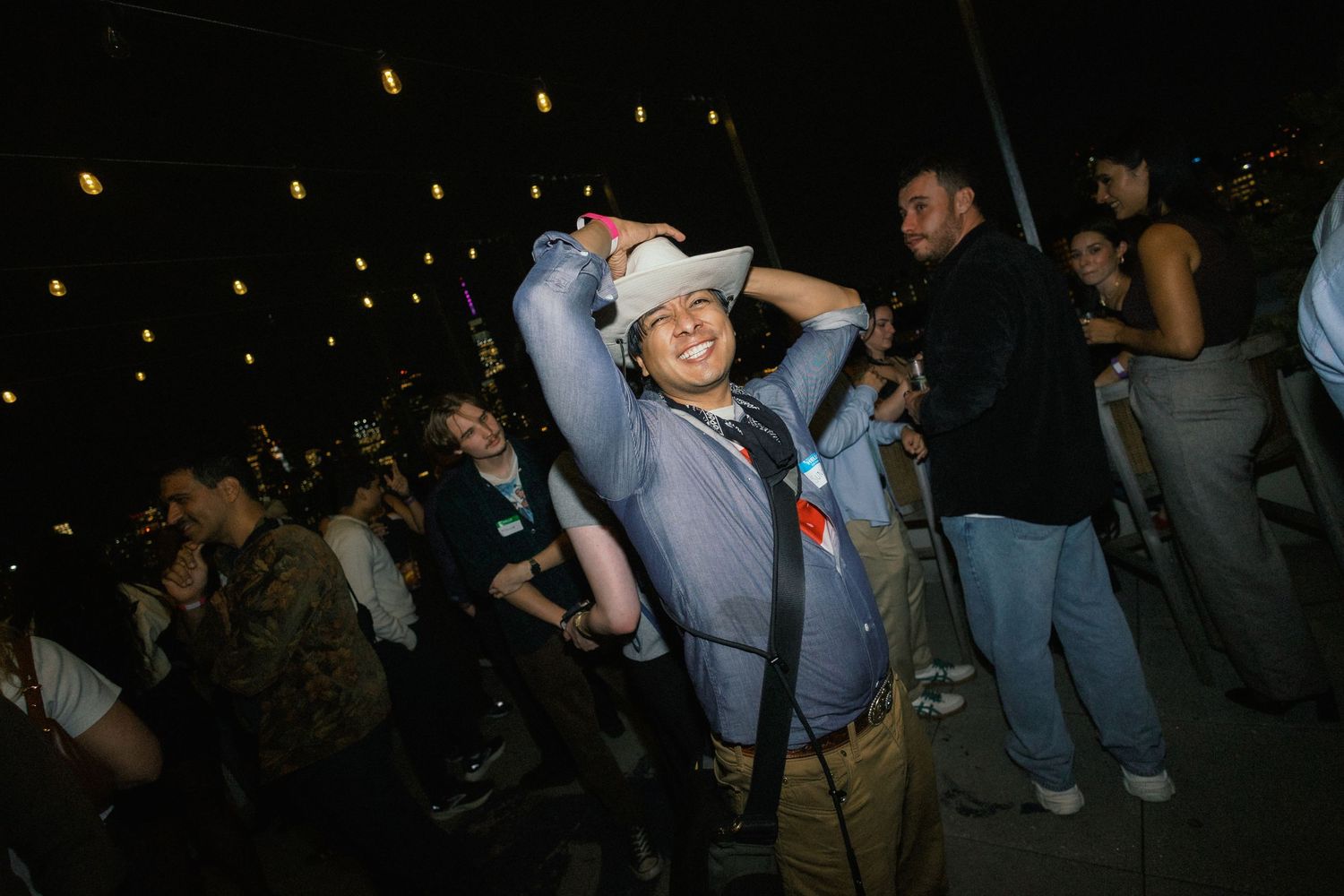 Person in white cowboy hat dancing joyfully at an outdoor nighttime event with crowd in background.