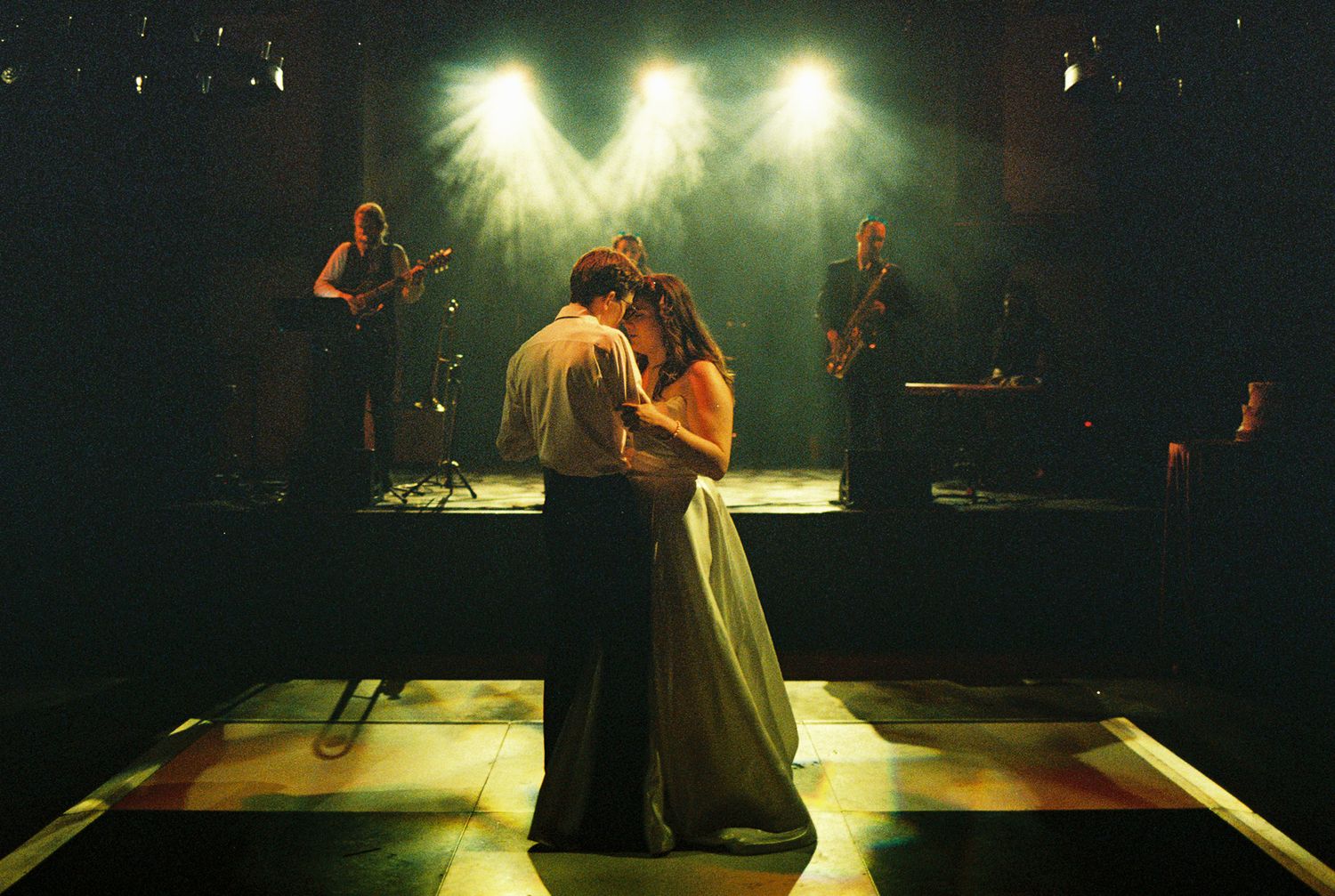 Couple sharing romantic dance on stage under spotlights with live band performing in background.